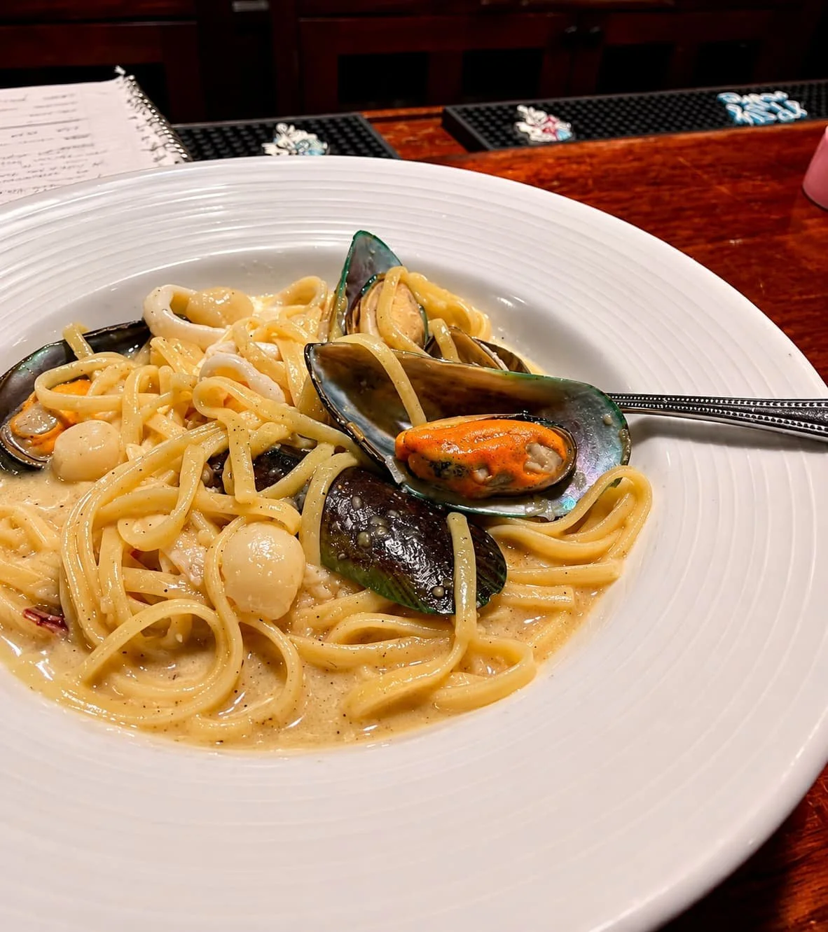 Plate of seafood pasta with mussels, scallops, and pasta in a creamy sauce on a table.
