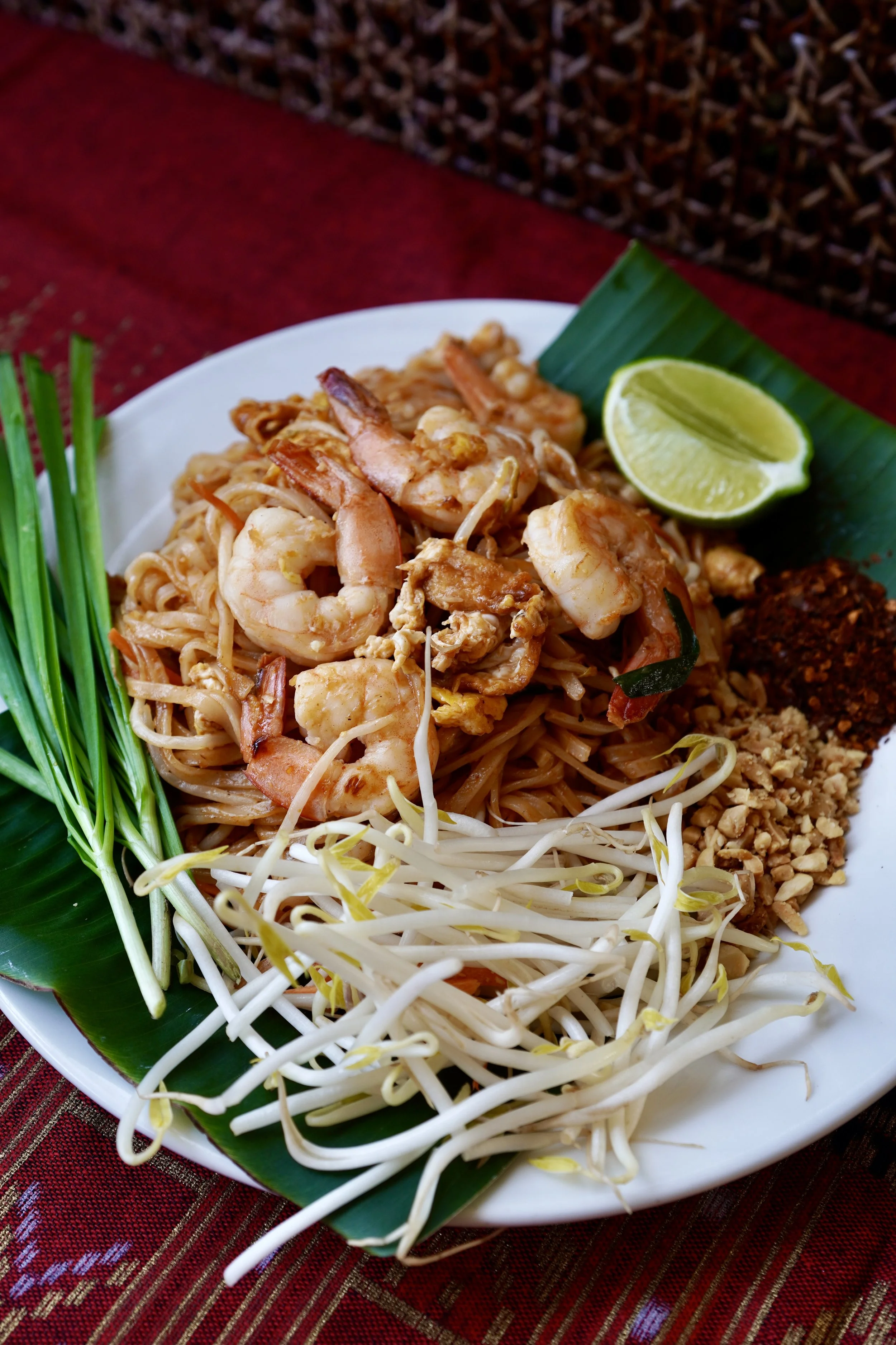 A plate of Pad Thai with shrimp, lime, bean sprouts, chopped peanuts, and green onions.