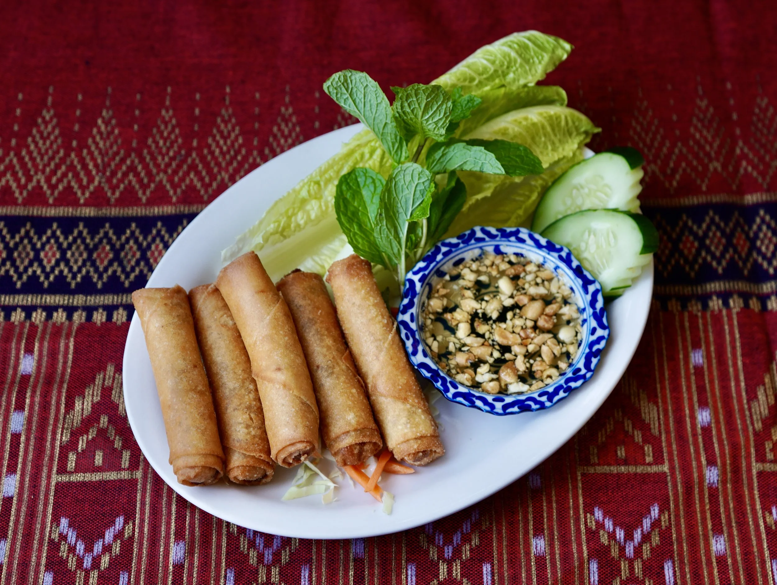 Plate of our Fried Spring Rolls served with cucumber slices, fresh mint, lettuce, and homemade peanut sauce.