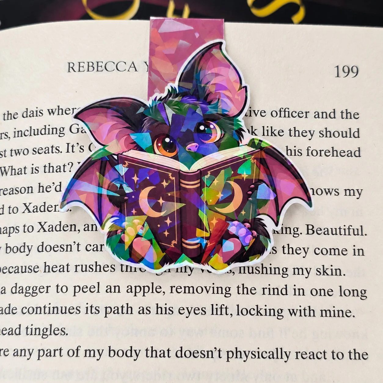 Holographic double-sided magnetic bookmark featuring a black bat reading a purple book decorated with gold moons and stars.