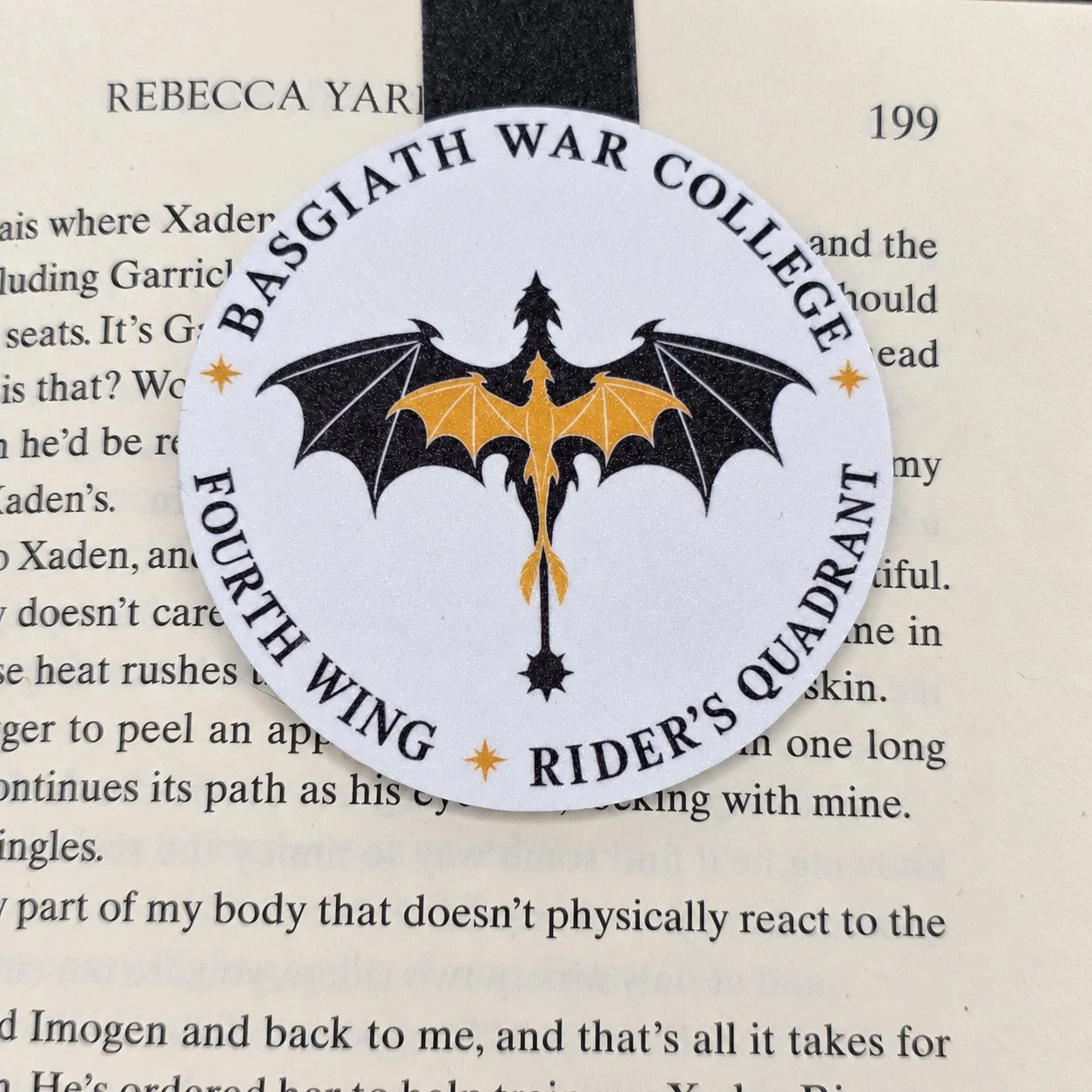 Double-sided magnetic bookmark featuring a circular Basgiath War College design with black and gold dragons, shown on a book page.