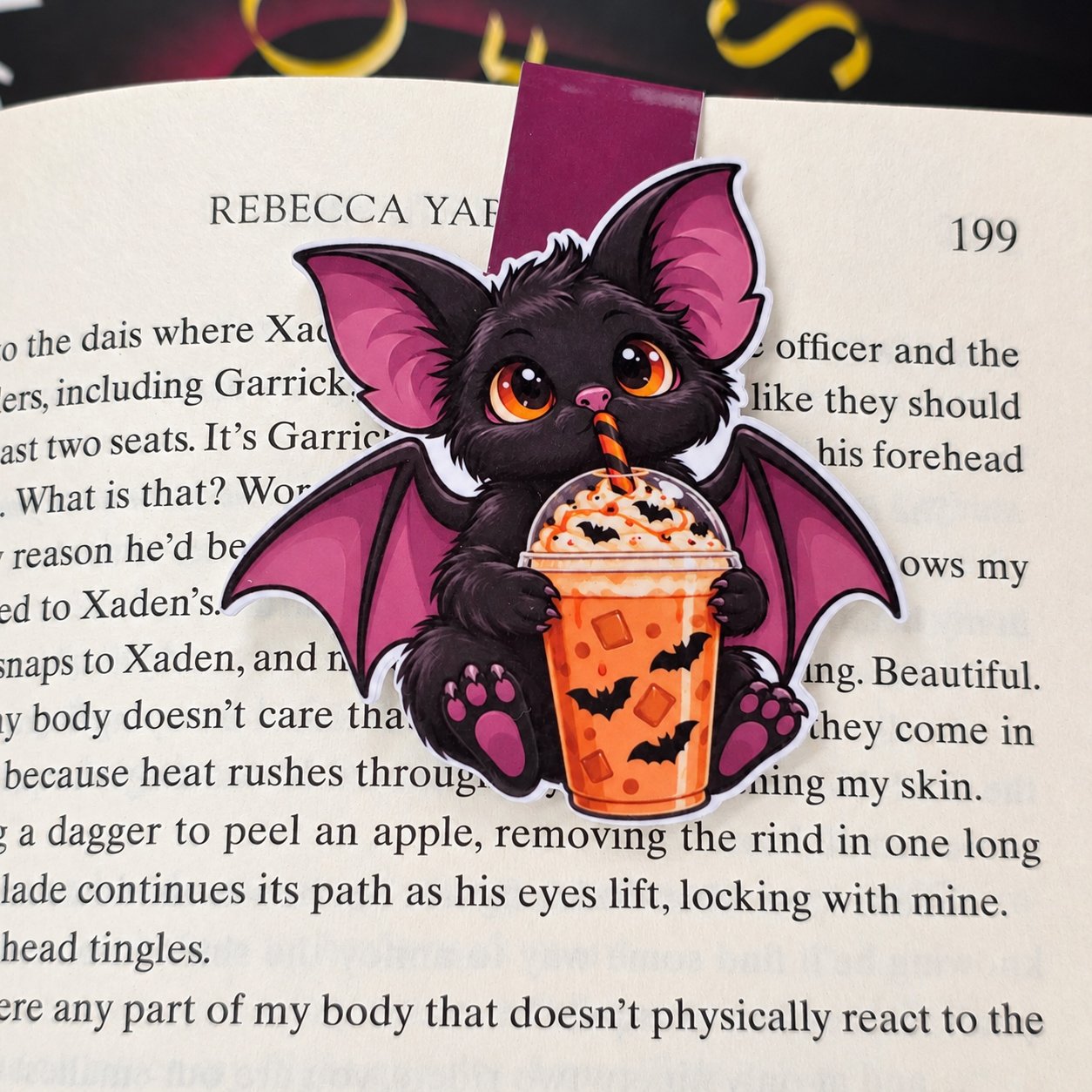 Double-sided magnetic bookmark featuring a black bat with purple wings holding an orange iced drink decorated with bats.