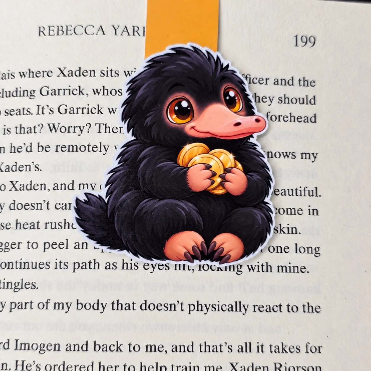 Double-sided magnetic bookmark featuring a fluffy black creature holding gold coins, with an orange tab.