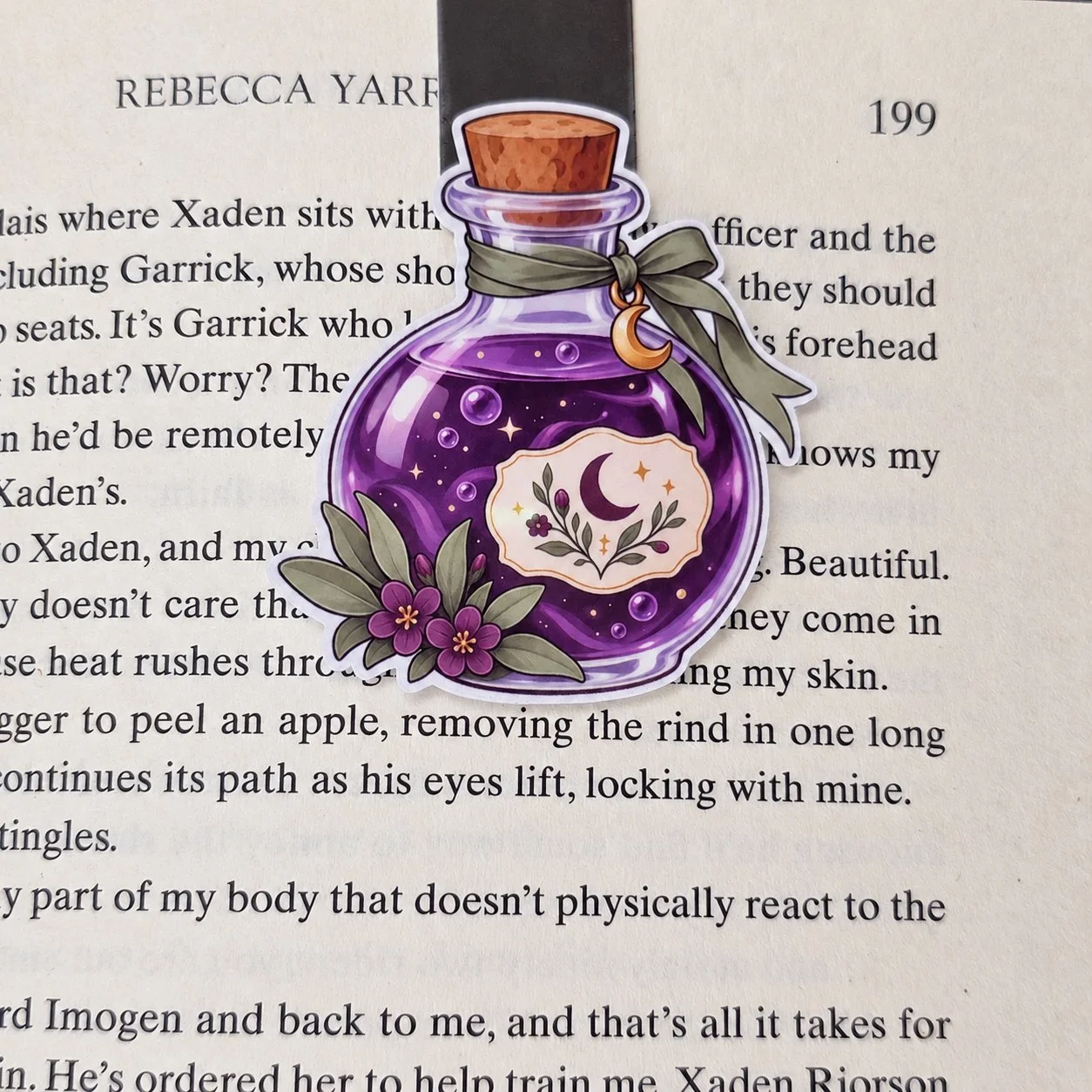 Double-sided magnetic bookmark featuring a purple potion bottle decorated with flowers, an olive ribbon, and a gold crescent moon charm.