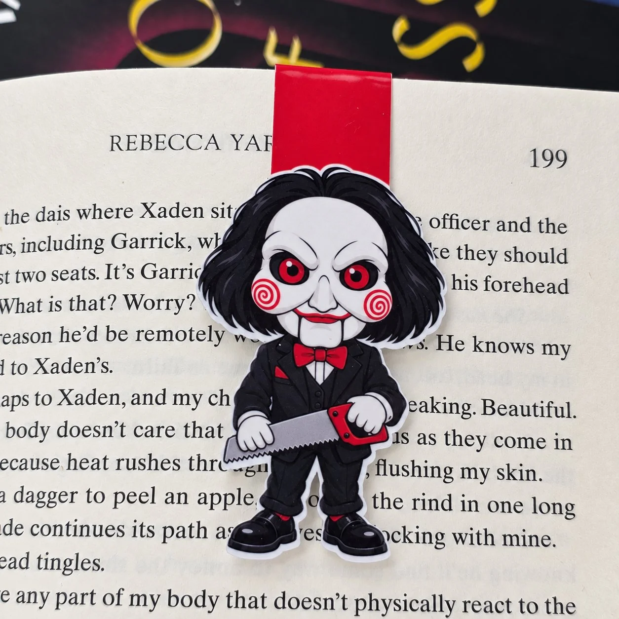 Double-sided magnetic bookmark featuring Billy the Puppet with red spiral cheeks, a black suit, and a red bow tie, holding a saw.