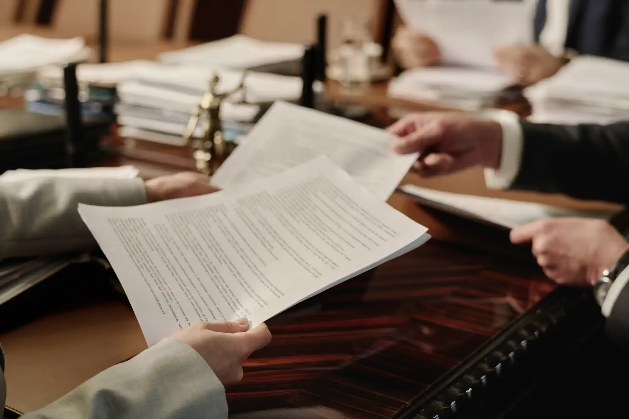 Personas intercambiando documentos legales u oficiales en una oficina o en una sala de tribunal, con pilas de papeles y expedientes sobre la mesa.