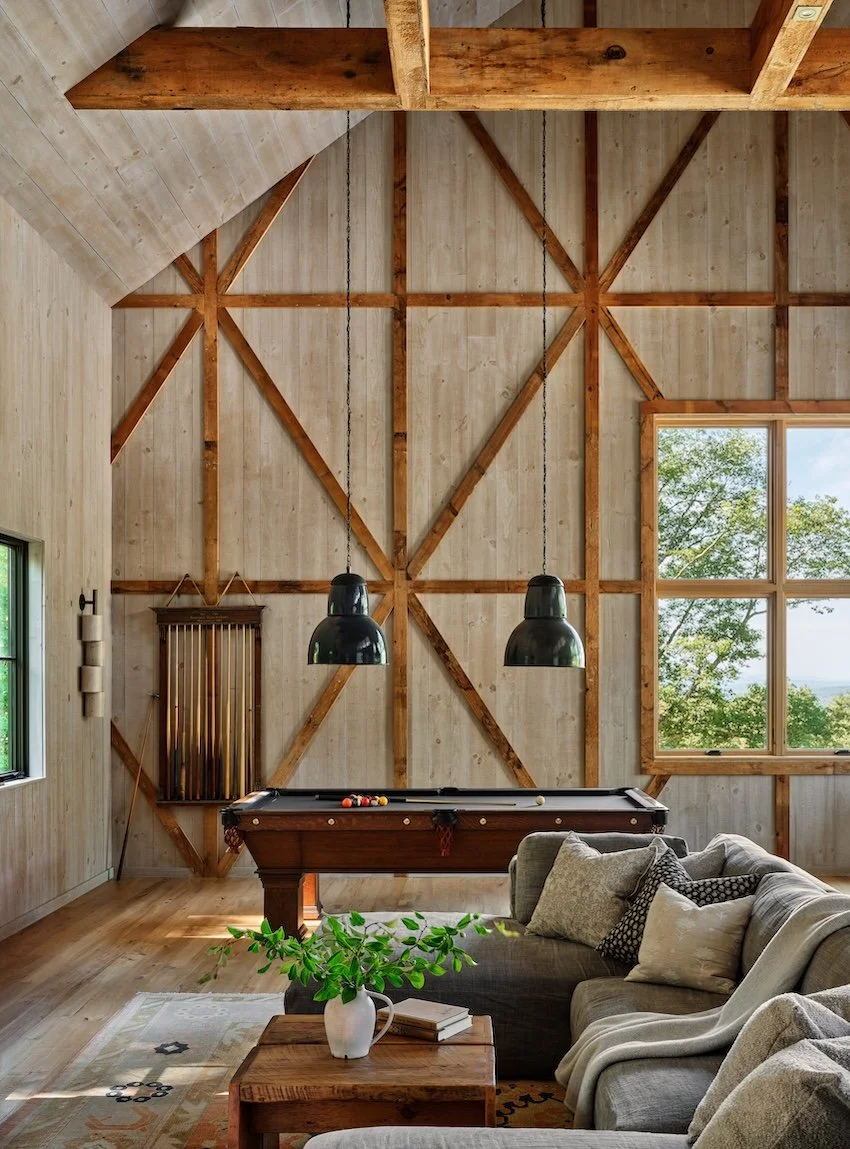 Game room in a renovated home in Dorset, Vermont, with a pool table, vaulted ceiling, exposed timber framing, and large windows.