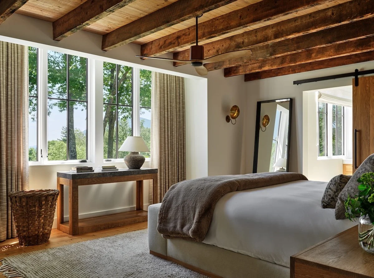 Bedroom in a renovated home in Dorset, Vermont, with exposed ceiling beams, large windows, and a wood console table.