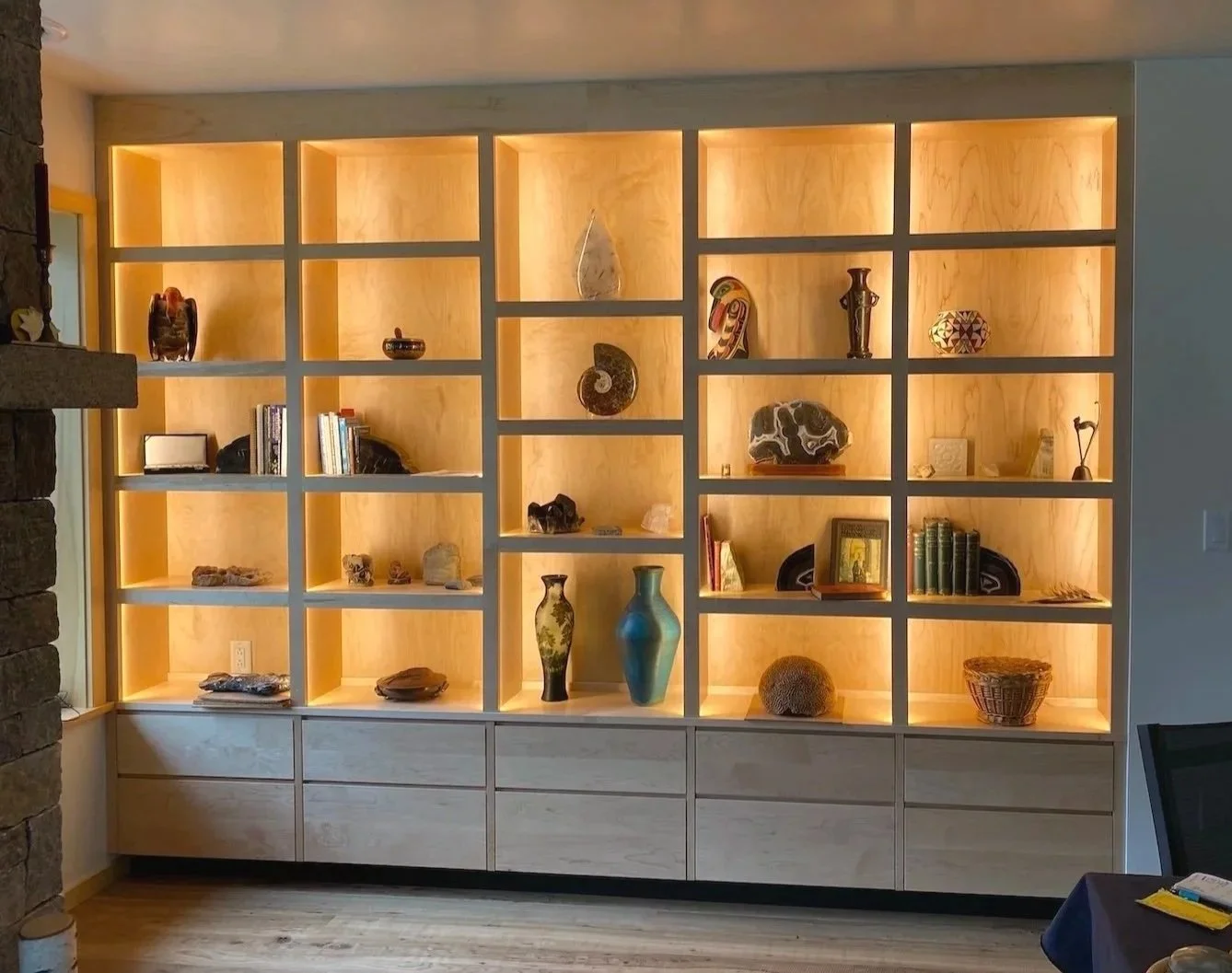 Built-in display shelving in a custom home in West Arlington, Vermont, with illuminated wood niches, lower cabinetry, and sculptural objects arranged throughout.