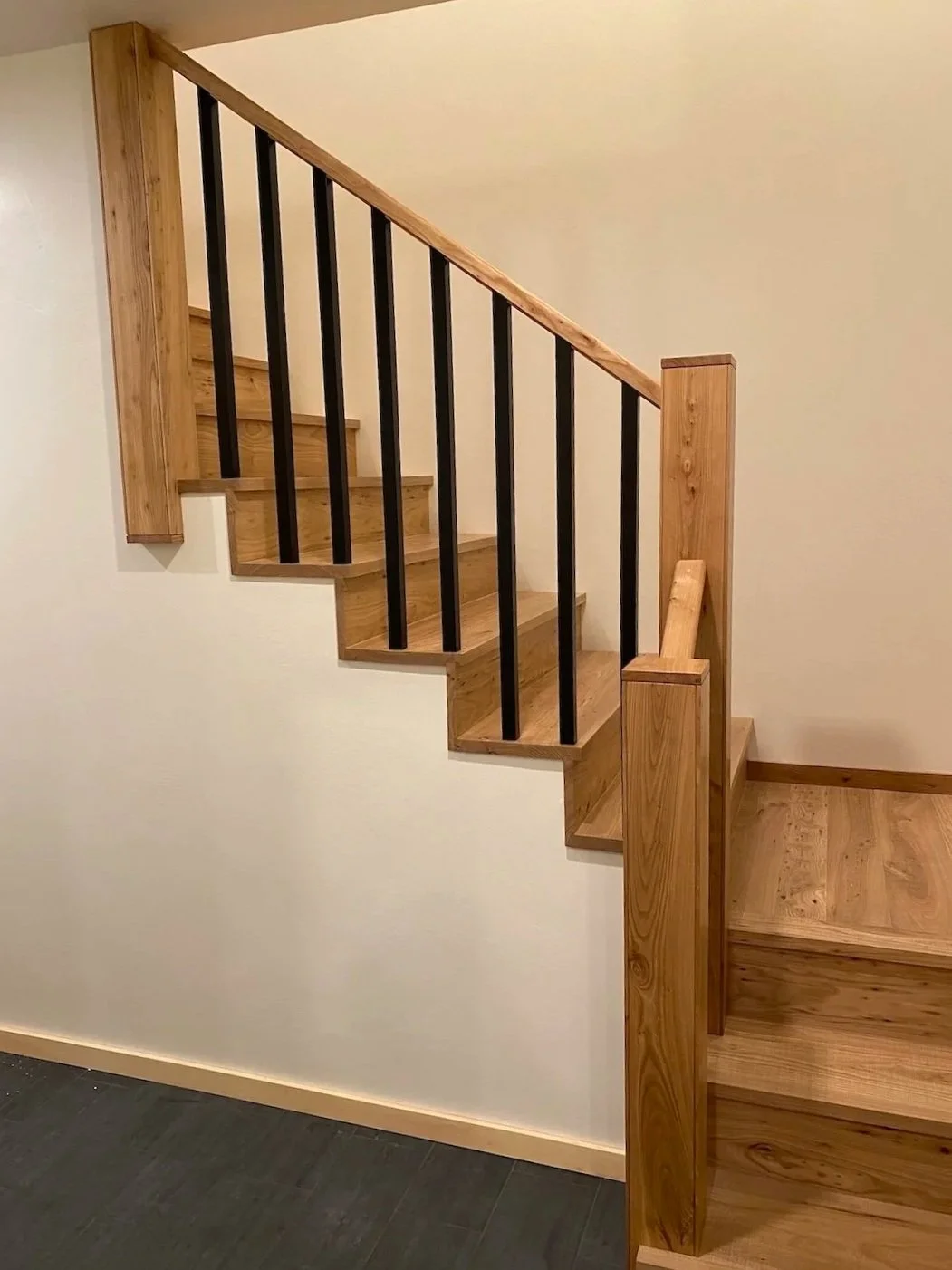 Wood staircase in a custom home in West Arlington, Vermont, with a light wood handrail, black balusters, and clean modern detailing.