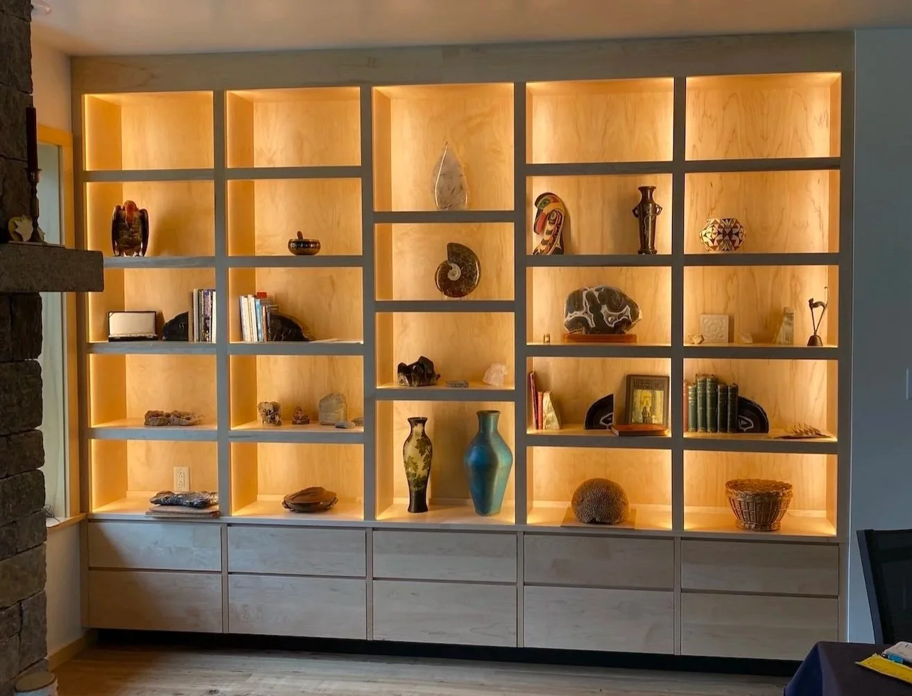 Built-in display shelving in a custom home in West Arlington, Vermont, with illuminated wood niches, lower cabinetry, and sculptural objects arranged throughout.