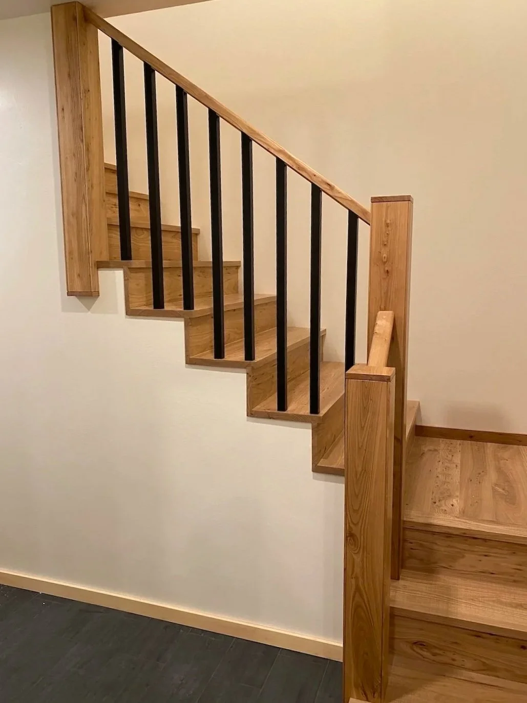 Wood staircase in a custom home in West Arlington, Vermont, with a light wood handrail, black balusters, and clean modern detailing.