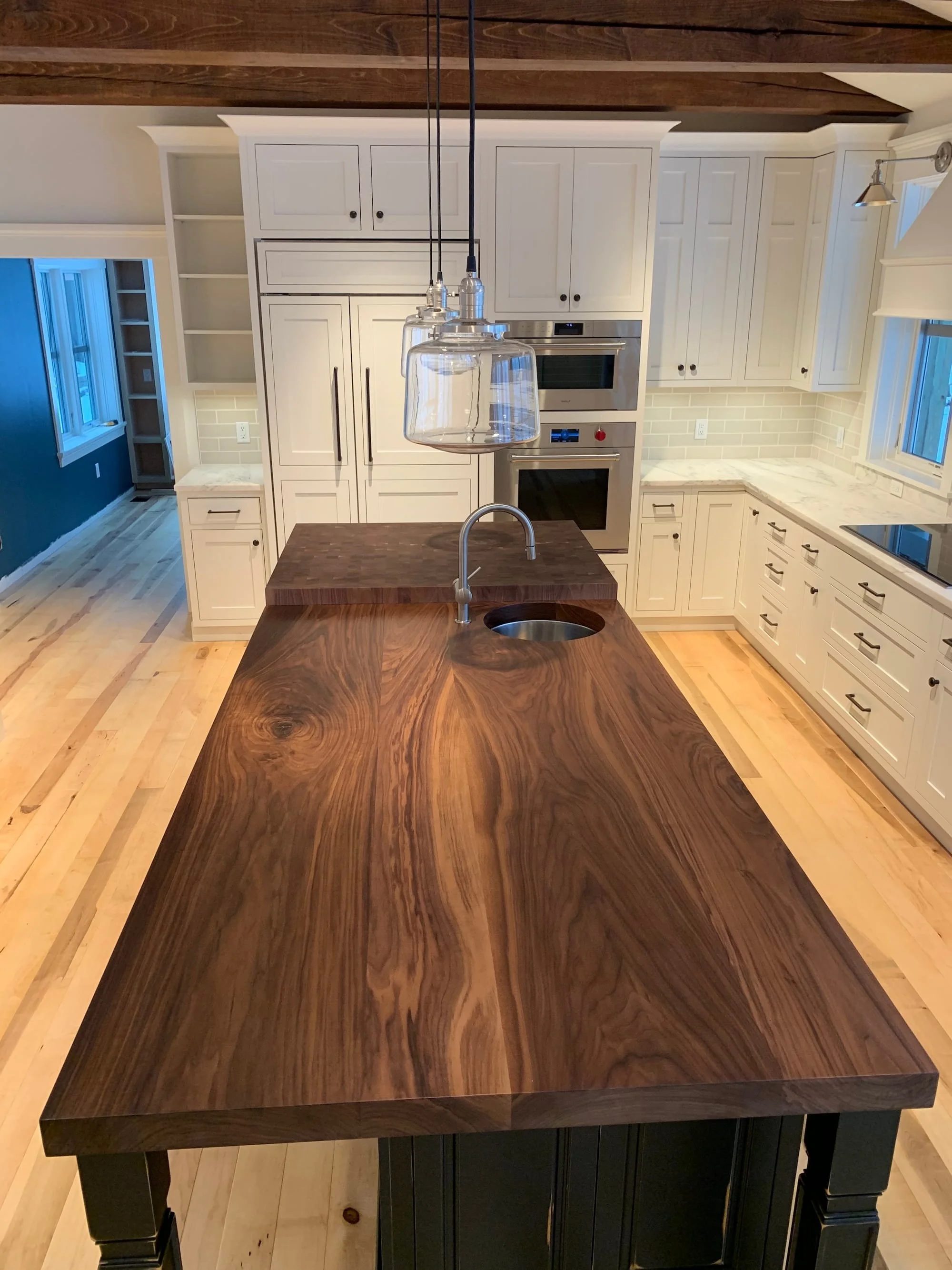 Kitchen in a custom home in Dorset, Vermont, with a large dark wood island, white cabinets, and light hardwood floors.