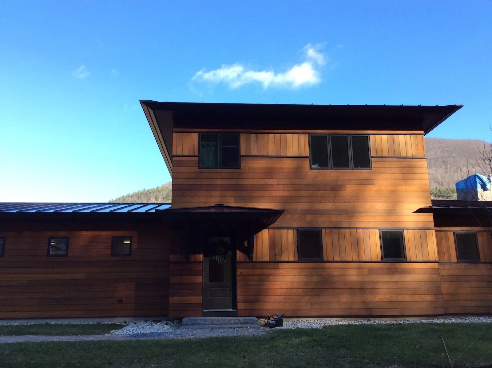 Exterior of a custom home in West Arlington, Vermont, with warm wood siding, a broad overhanging roof, and a simple horizontal form set against the landscape.