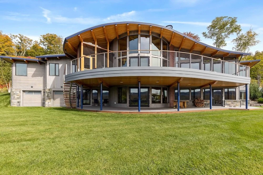 Rear exterior of a custom home in Wilmington, Vermont, with a curved roofline, wraparound deck, and expansive glass facing the mountain landscape.