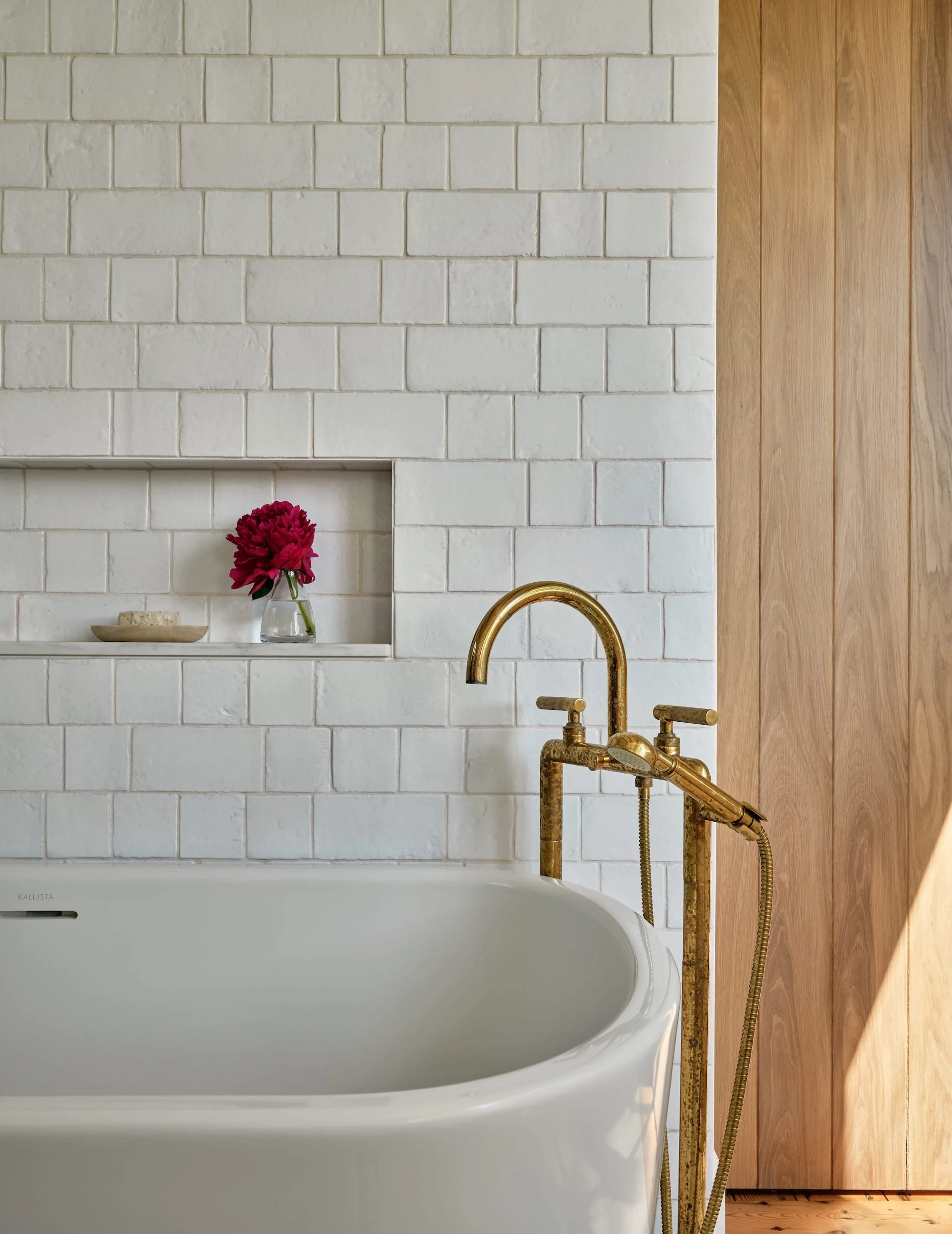 Bathroom in a renovated home in Dorset, Vermont, with a soaking tub, white tile walls, and a brass tub filler.