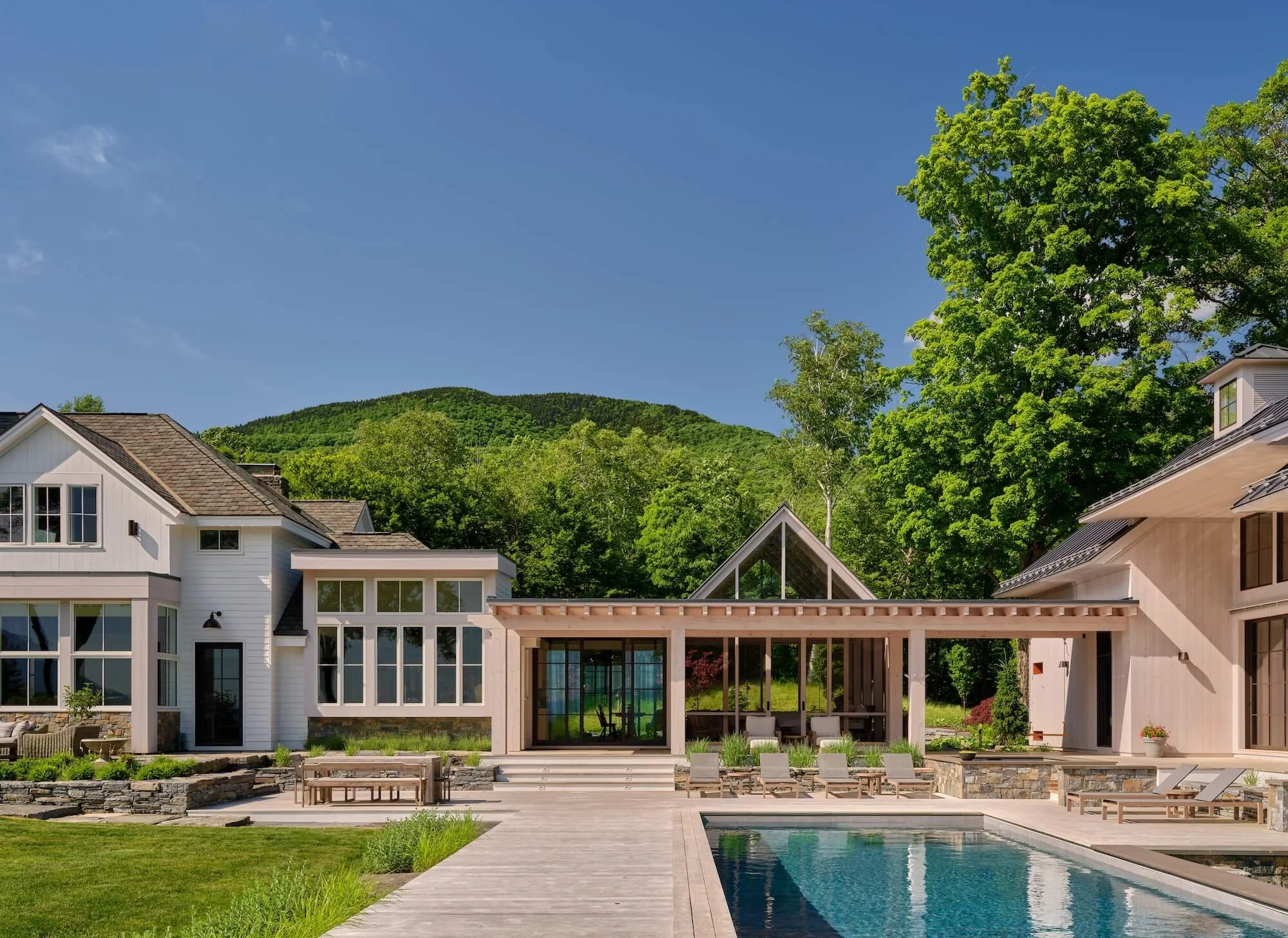 Exterior of a renovated home in Dorset, Vermont, with a pool, landscaped walkway, expansive windows, and adjacent guest barn.