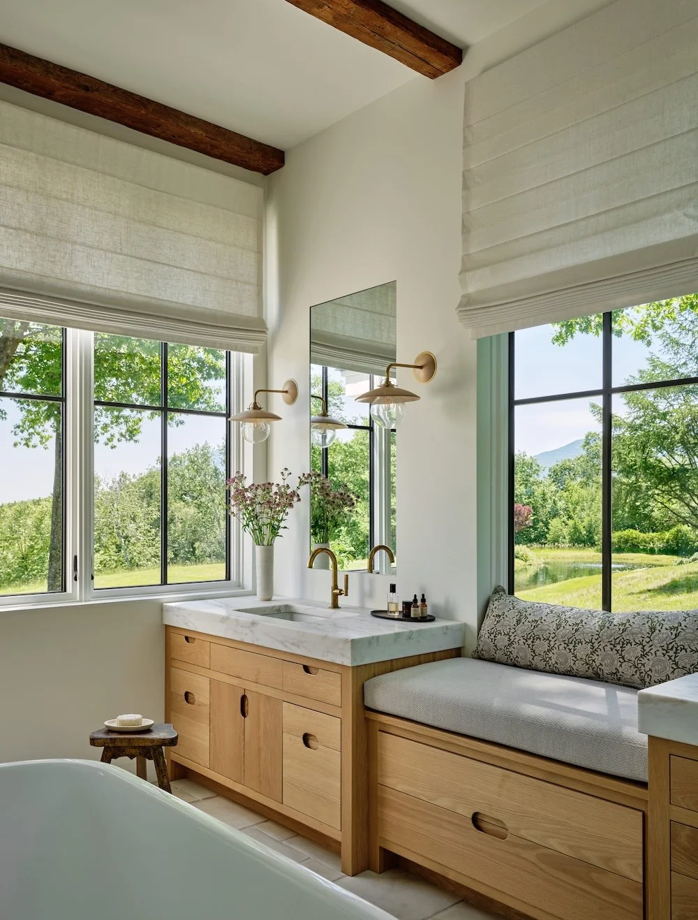 Bathroom in a custom home in Wilmington, Vermont, with a soaking tub, wood vanity, window seat, and large windows overlooking the landscape.