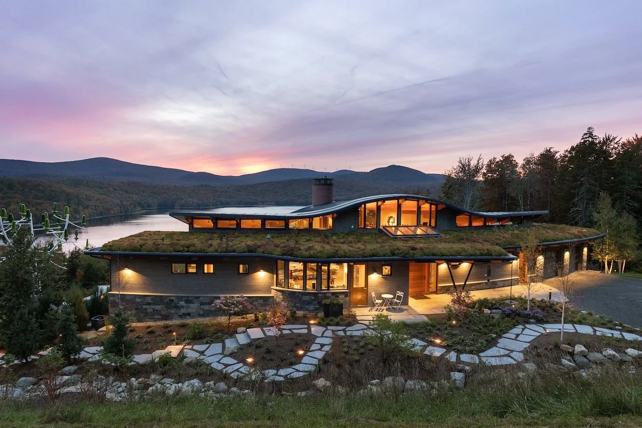 Dusk view of a custom home in Wilmington, Vermont, set into a hillside above the lake with curved architecture and illuminated interior spaces.