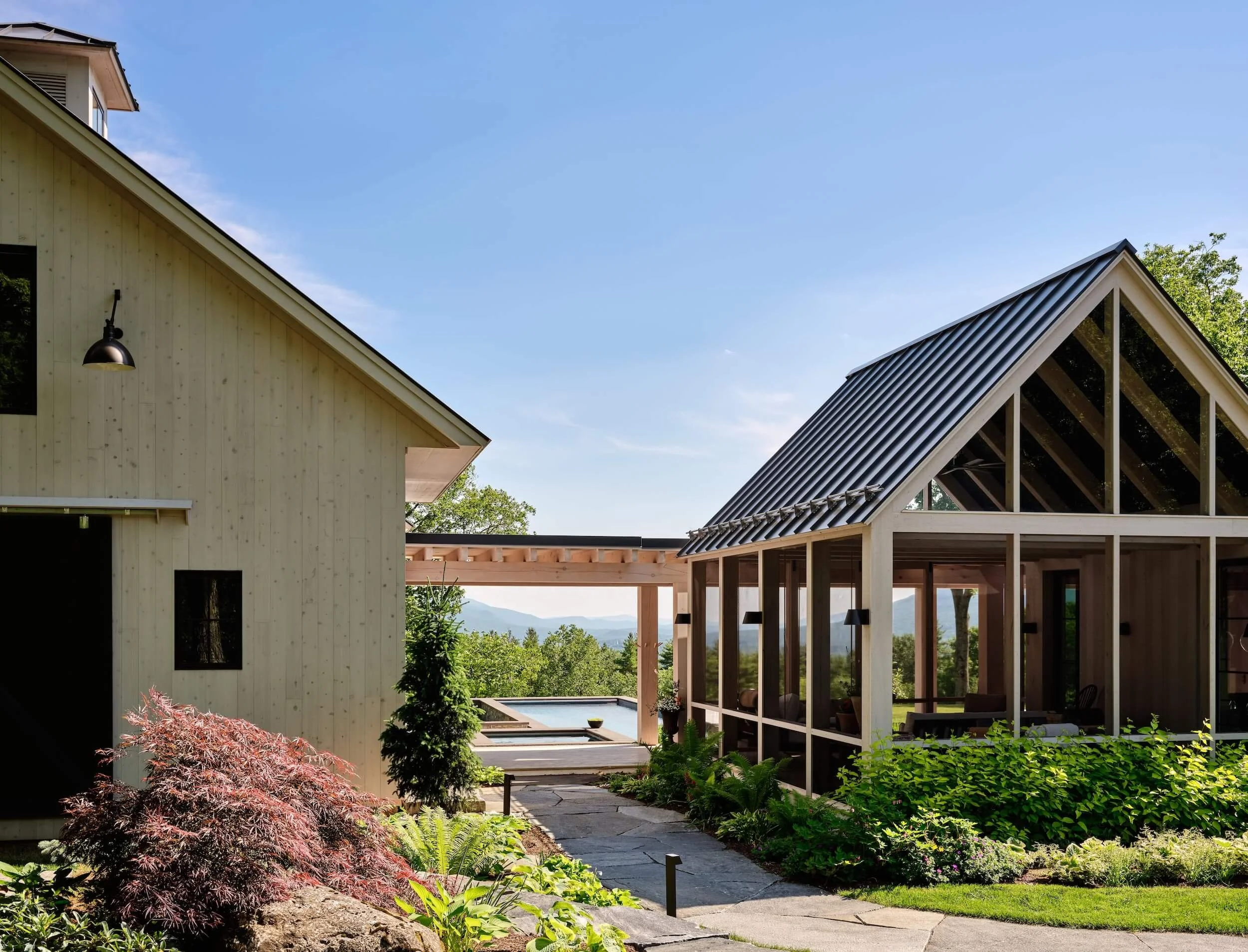 Exterior of a renovated home in Dorset, Vermont, with a landscaped stone walkway between two gabled structures, opening to distant mountain views beyond.
