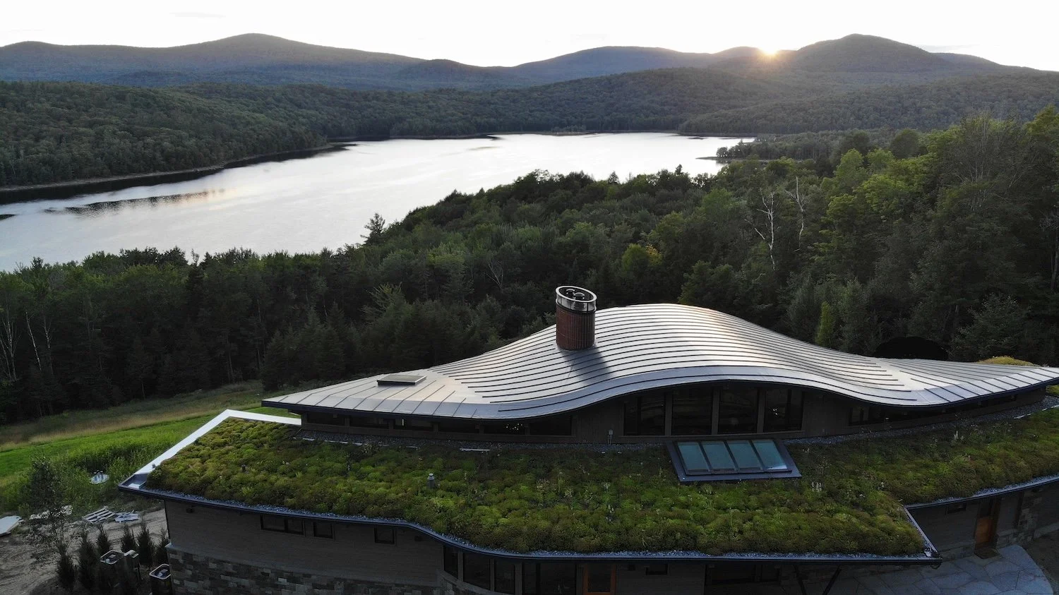 Aerial view of a custom home in Wilmington, Vermont, with a sweeping curved roof set against the lake and mountain landscape.