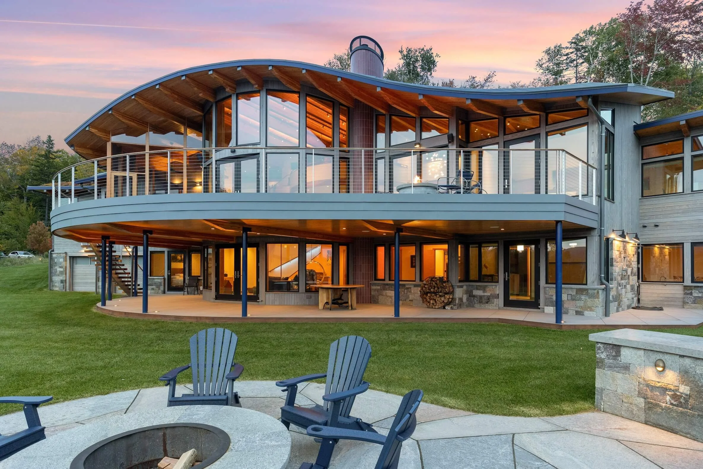 Rear exterior of a custom home in Wilmington, Vermont, with stone cladding, deep roof overhangs, and views toward the lake.