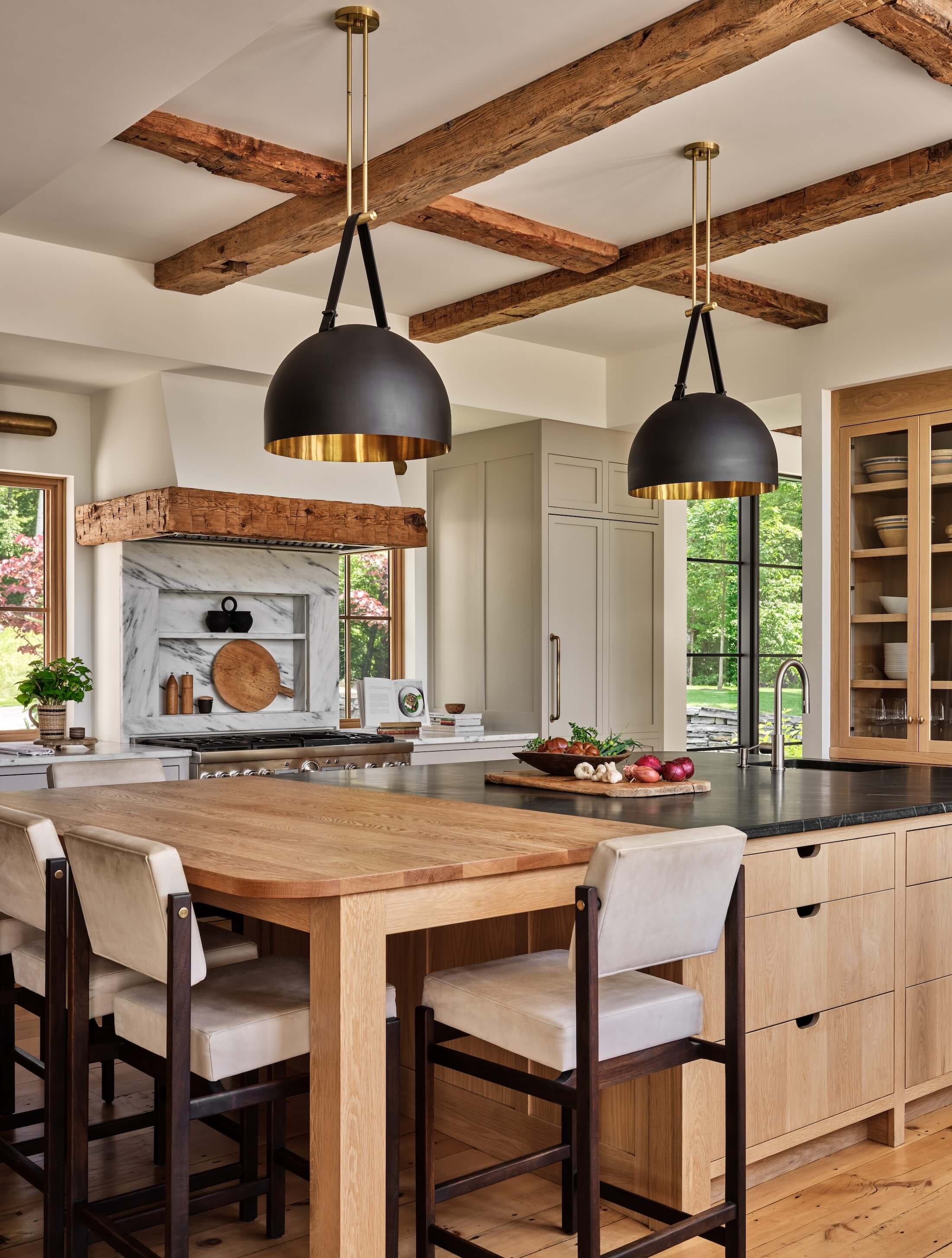 Kitchen in a renovated home in Dorset, Vermont, with a large wood island, light wood cabinetry, black pendant lights, and exposed ceiling beams.