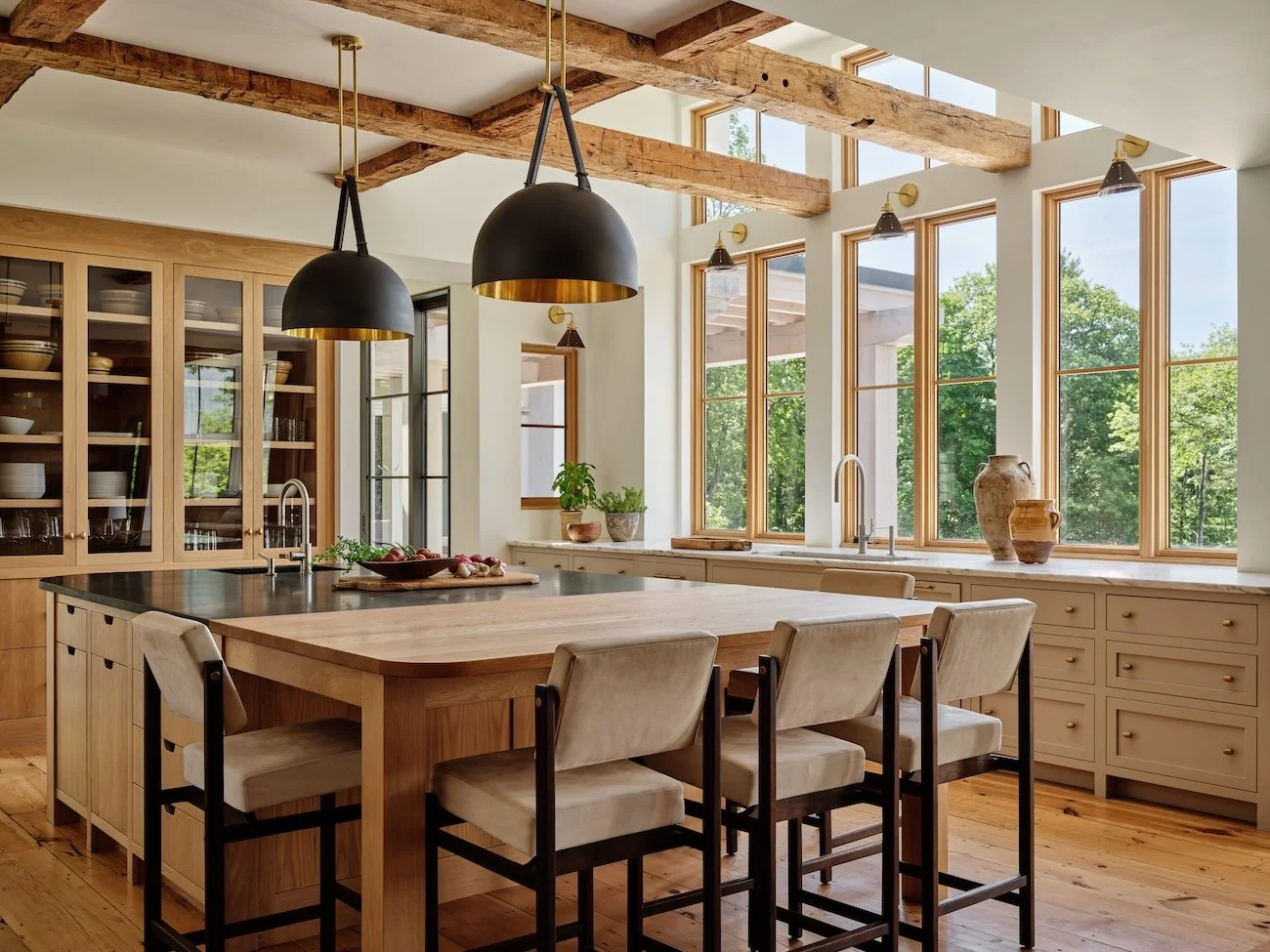 Kitchen in a renovated home in Dorset, Vermont, with a large island, wood cabinetry, black pendant lights, and expansive windows.