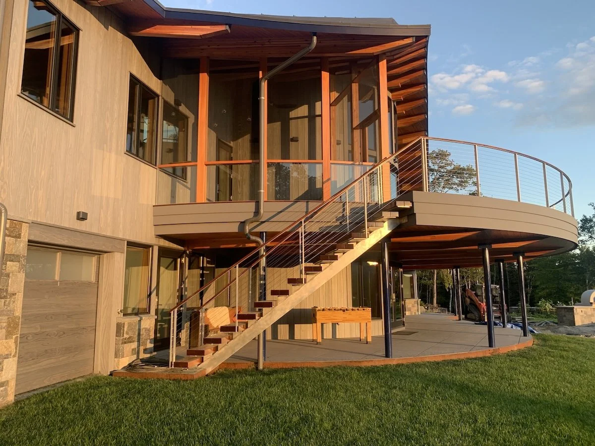 Side exterior of a custom home in Wilmington, Vermont, with curved decks, exterior stairs, and rounded forms echoing the architecture of the house.