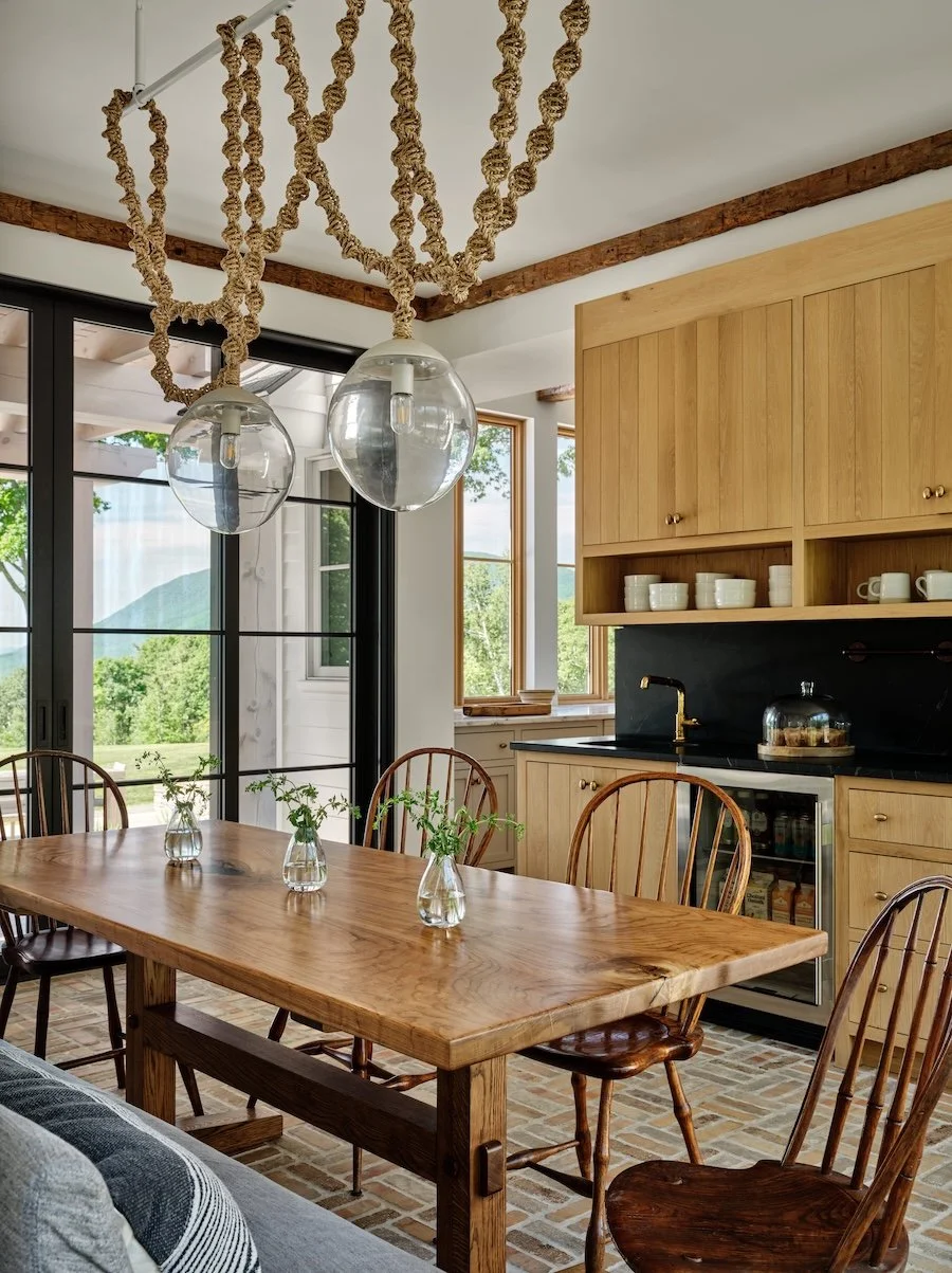 Dining area in a renovated home in Dorset, Vermont, with a wood table, light wood cabinetry, glass pendant lighting, and an open connection to the kitchen.