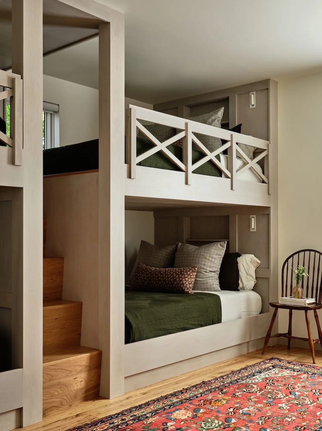 Bunk room in a renovated home in Dorset, Vermont, with built-in bunks, wood stairs, and a patterned area rug.