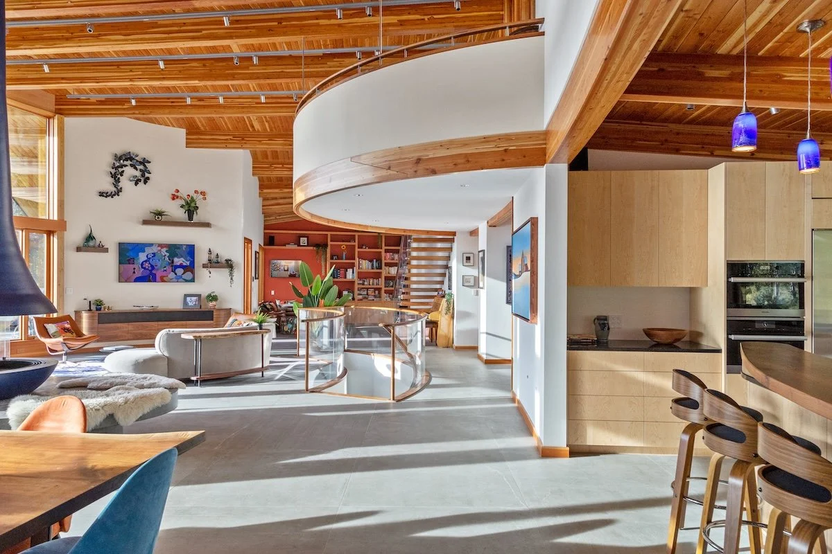 Main living area in a custom home in Wilmington, Vermont, with curved interior architecture, wood ceilings, a circular upper-level loft, and abundant natural light.