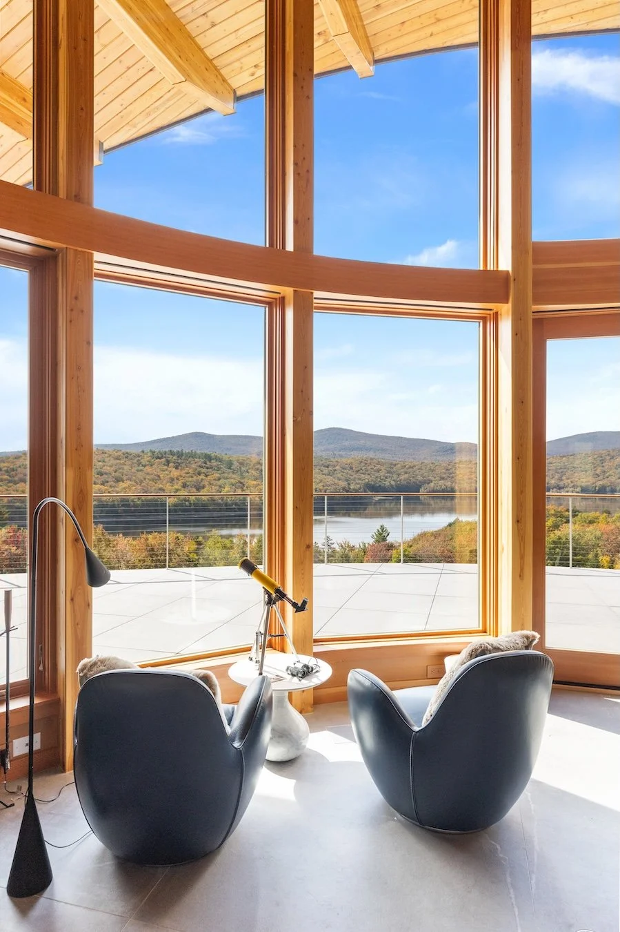 Curved wall of wood-framed windows in a custom home in Wilmington, Vermont, opening to broad views of the lake and surrounding mountains.