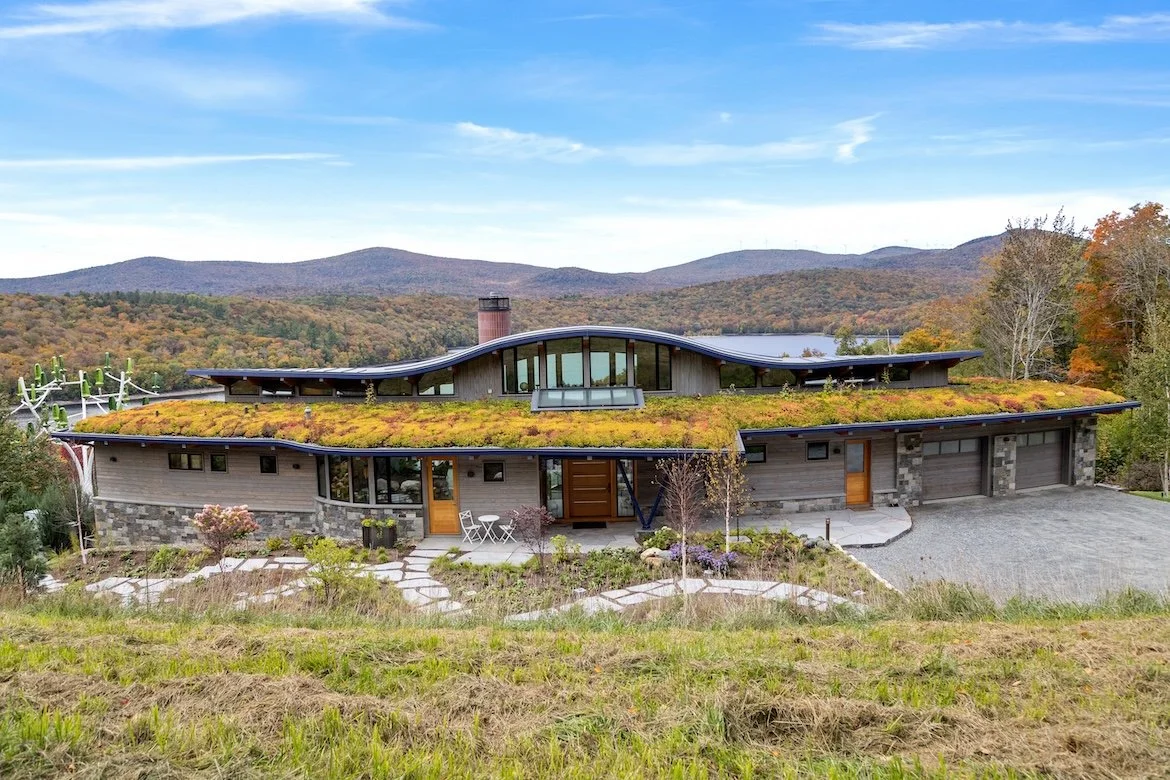 Front elevation of a custom home in Wilmington, Vermont, with a planted roof, curved geometry, and a long low profile set into the hillside.