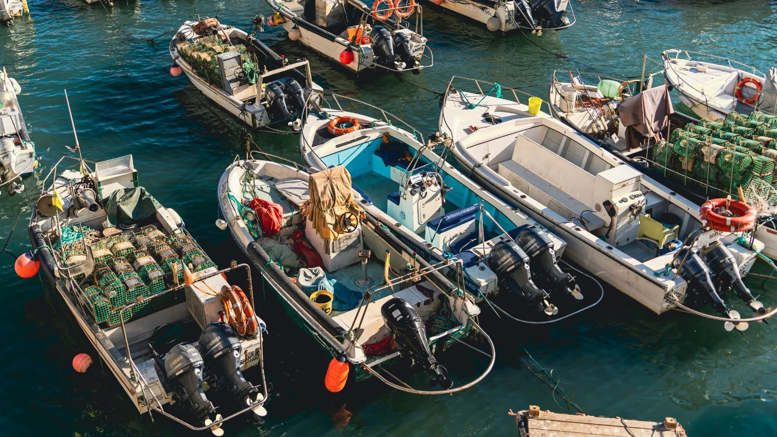 Several small boats docked together in a harbor, equipped with fishing gear and engines.