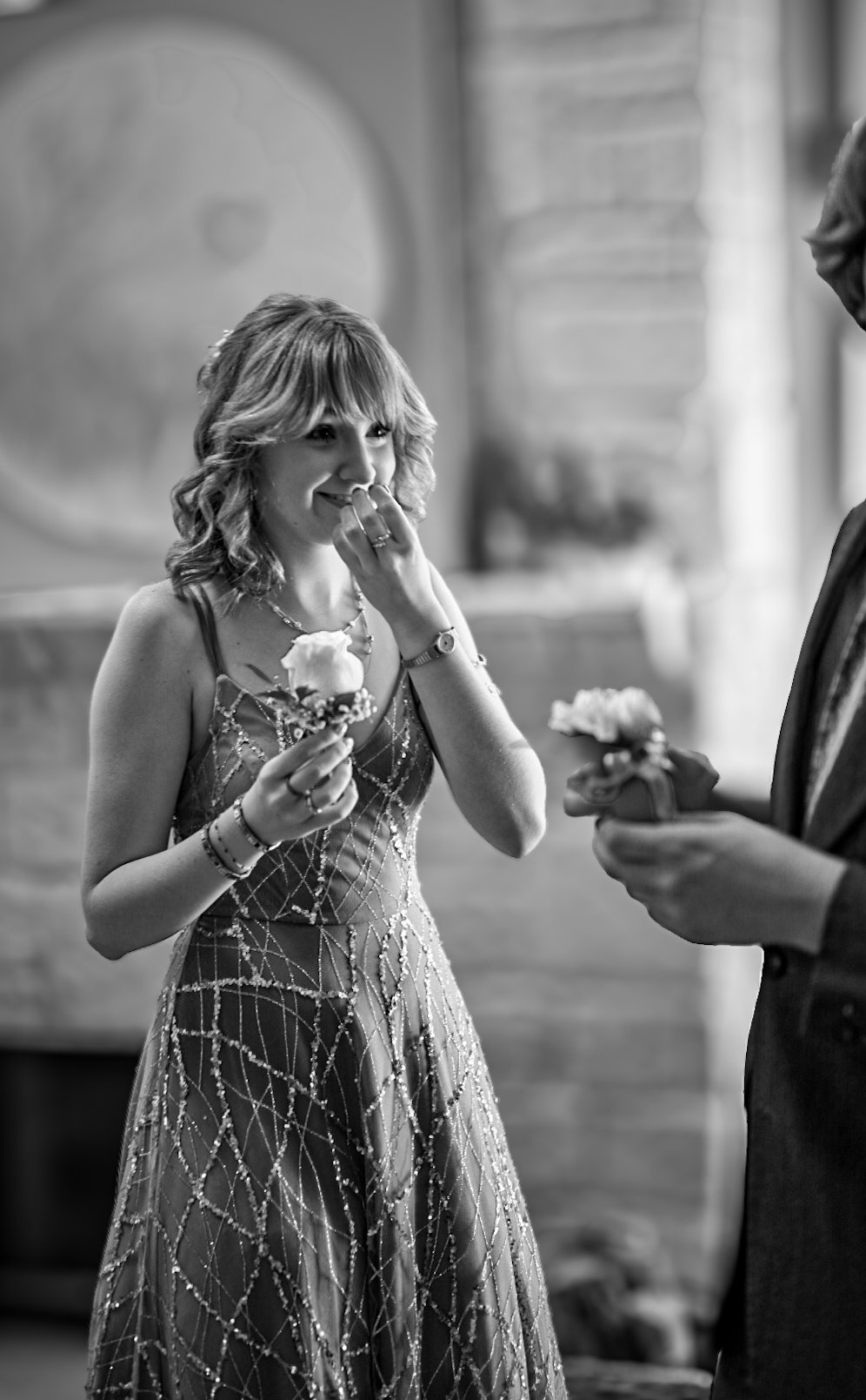 A pretty blond girl wearing a prom dress with sequins reacts to being given a corsage by a boy