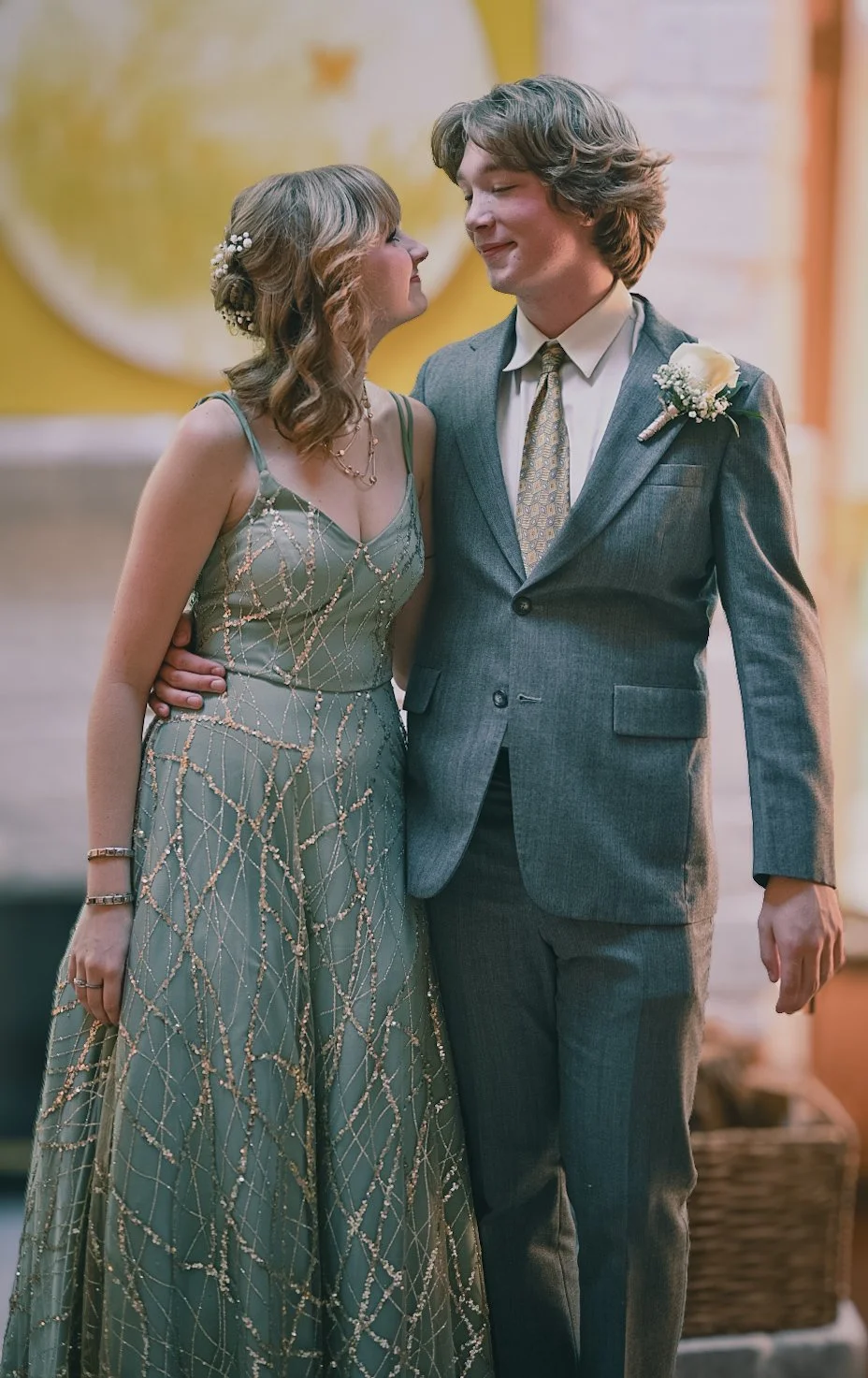 a teenage couple dressed in a suit and prom dress smiling at each other