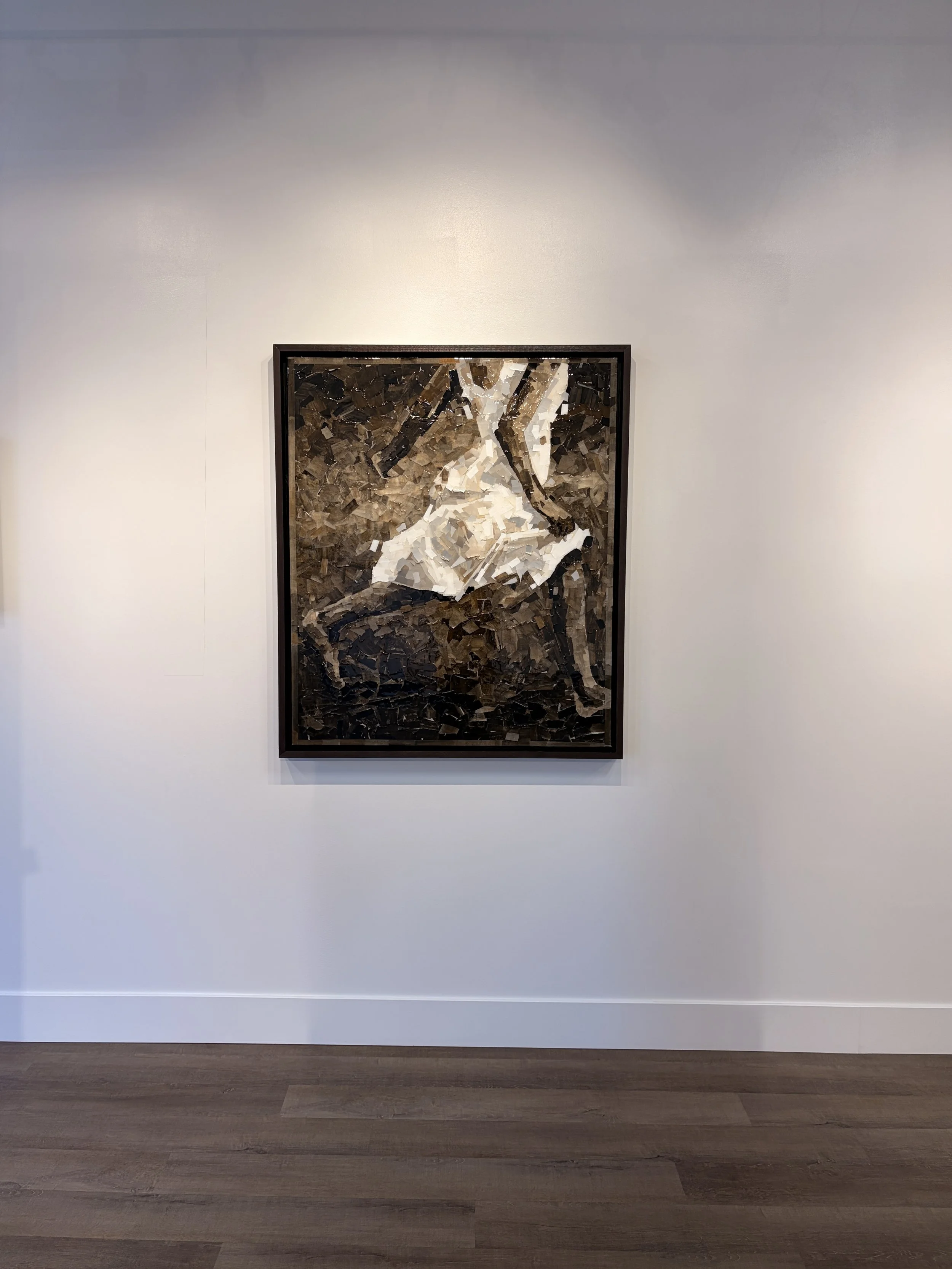 A framed abstract mixed media painting featuring a figure in a white dress, situated on a white gallery wall with wooden flooring.