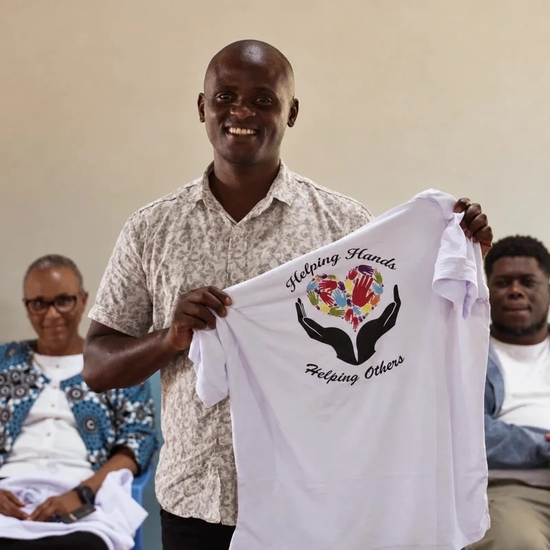 A local leader holding a white T-shirt with the words "Helping Hands Helping Others" written on it. Picture taken during the inaugural event of the Ndithini vocational school.