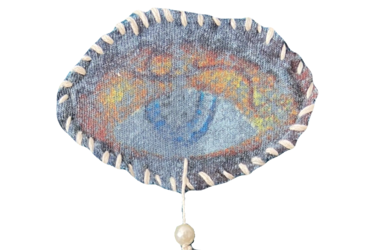 Close-up of a circular woven fabric with an embroidered eye pattern in the center, surrounded by a border of white stitches.