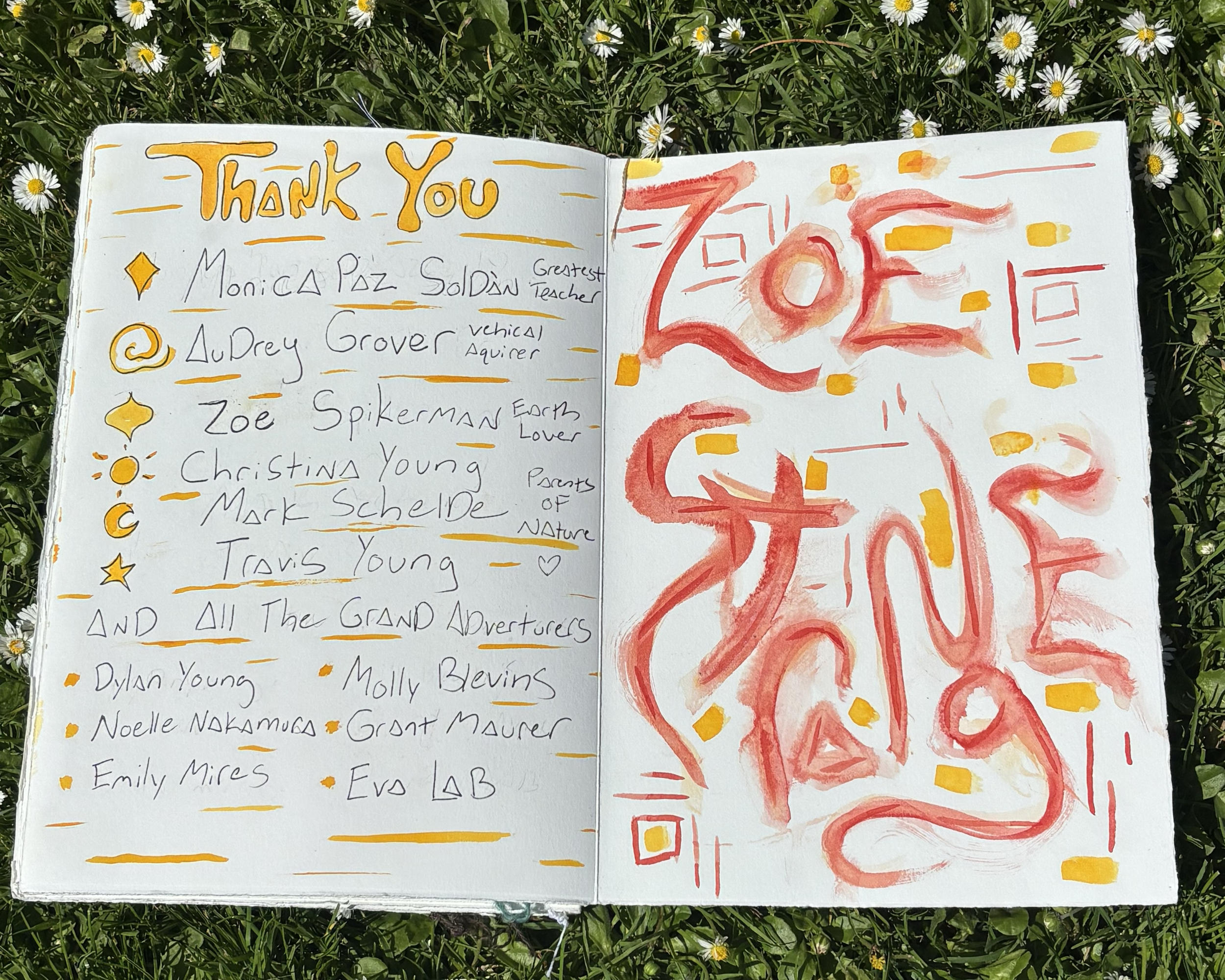 Open notebook with handwritten thank you note on left page and abstract red and yellow painted design on right page, lying on grass with small white daisies.