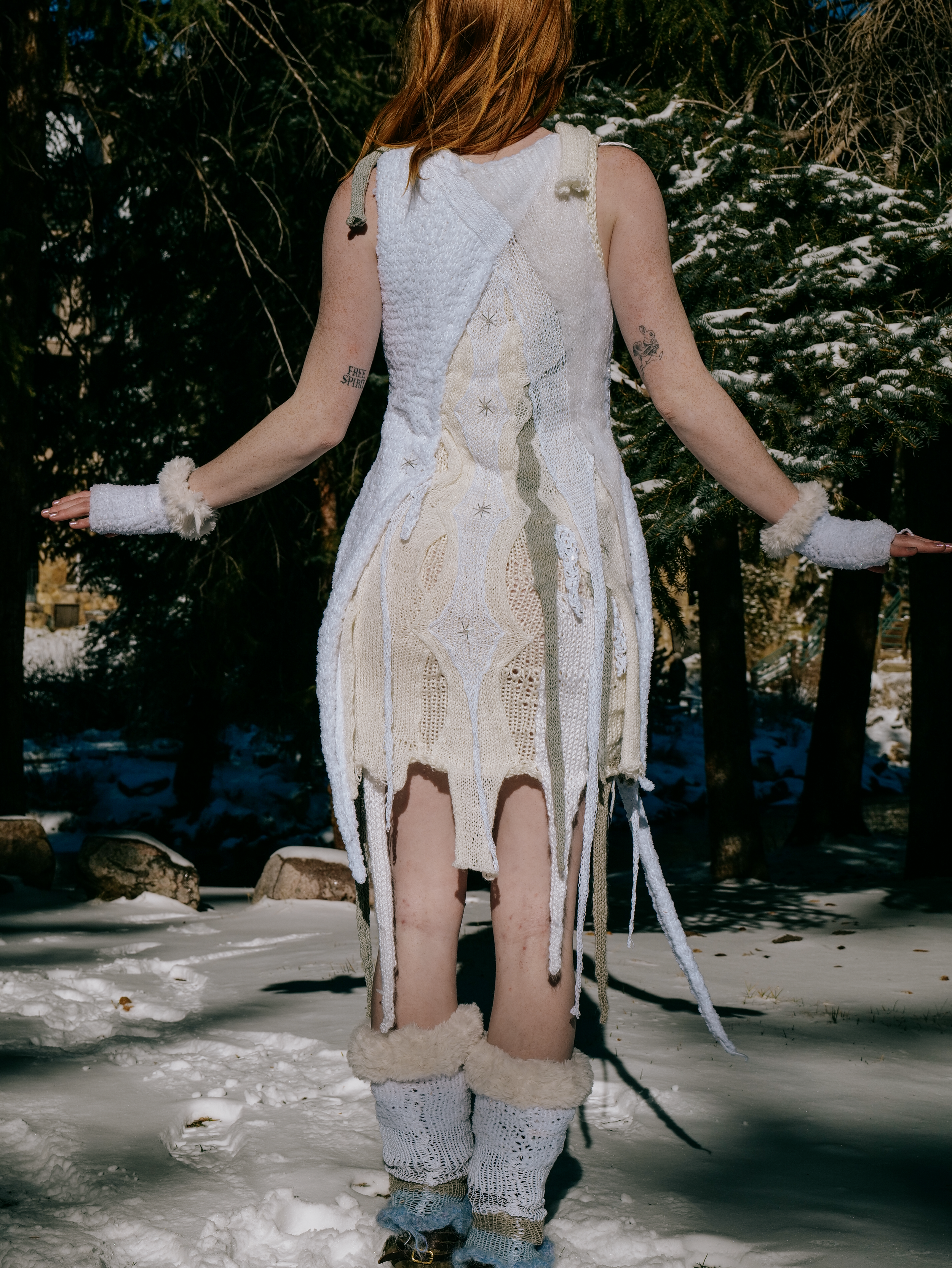 A woman standing outdoors in snow, wearing a handmade, knitted, and crocheted dress with matching wrist and leg warmers.