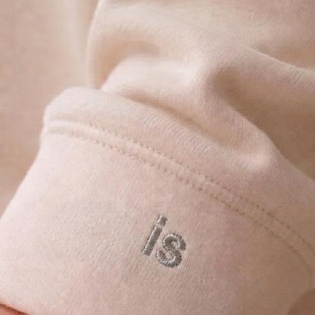 Close-up of a light creme coloured sweatshirt with the word 'is' embroidered near the sleeve.
