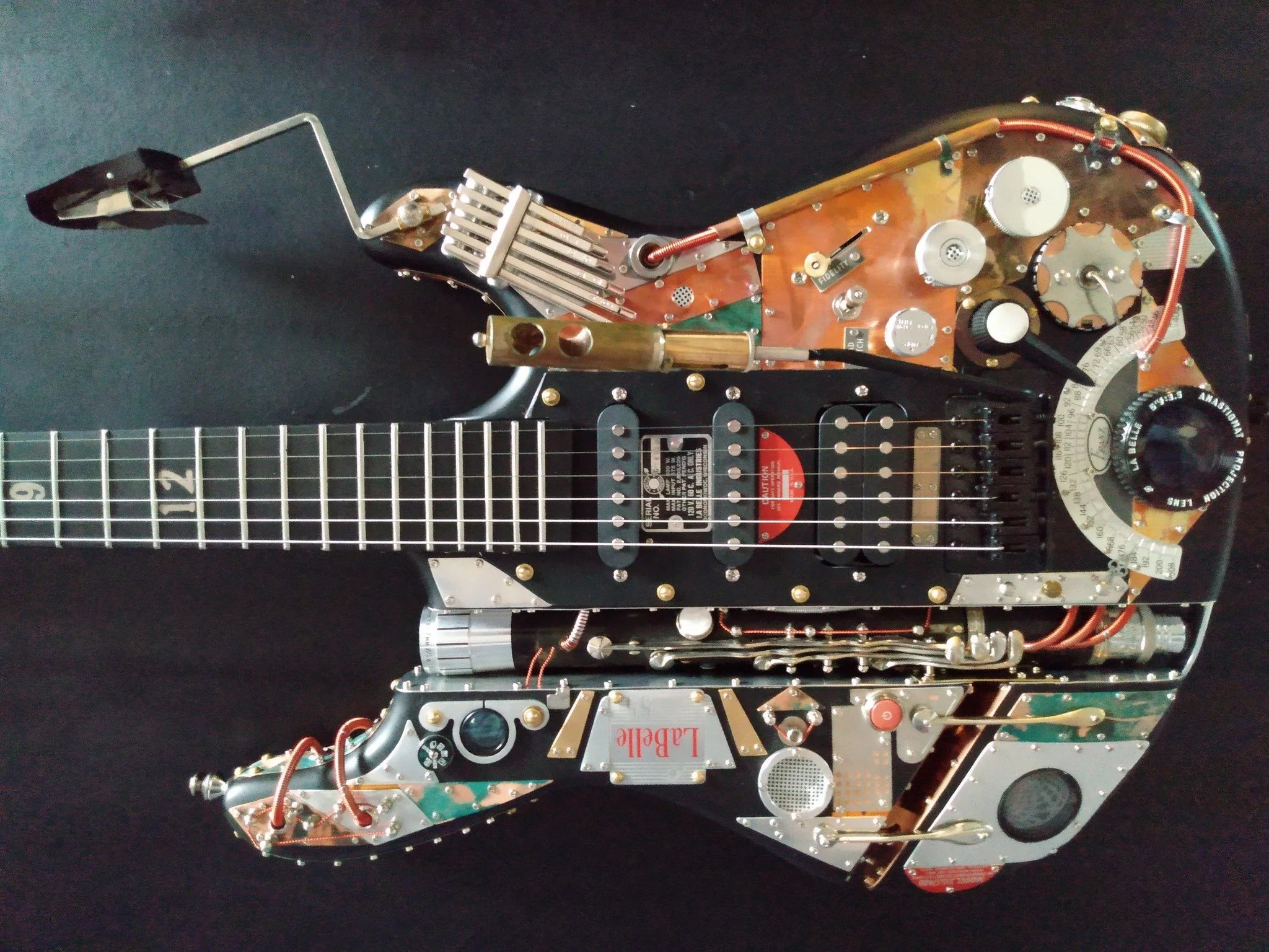 The LaBelle 55, named for vintage parts from 1955 LaBelle slide projector  Made by Mike Moulton, luthier atImmortal Guitars.Sounds and plays great. Also used clarinet parts. Flat black with burnished copper, aluminum, Steampunk Guitar. Attached lyre.