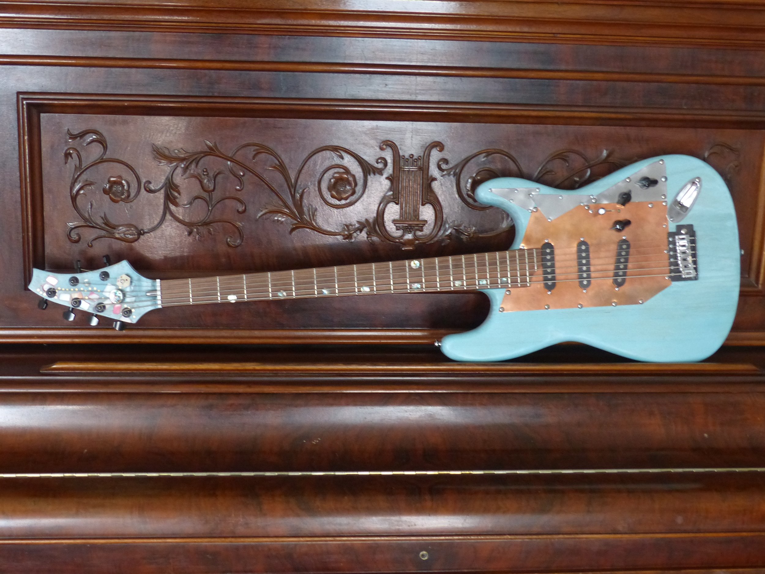 6 string bass, sitting on vintage upright grand piano, custom one of a kind by Immortal Guitars.