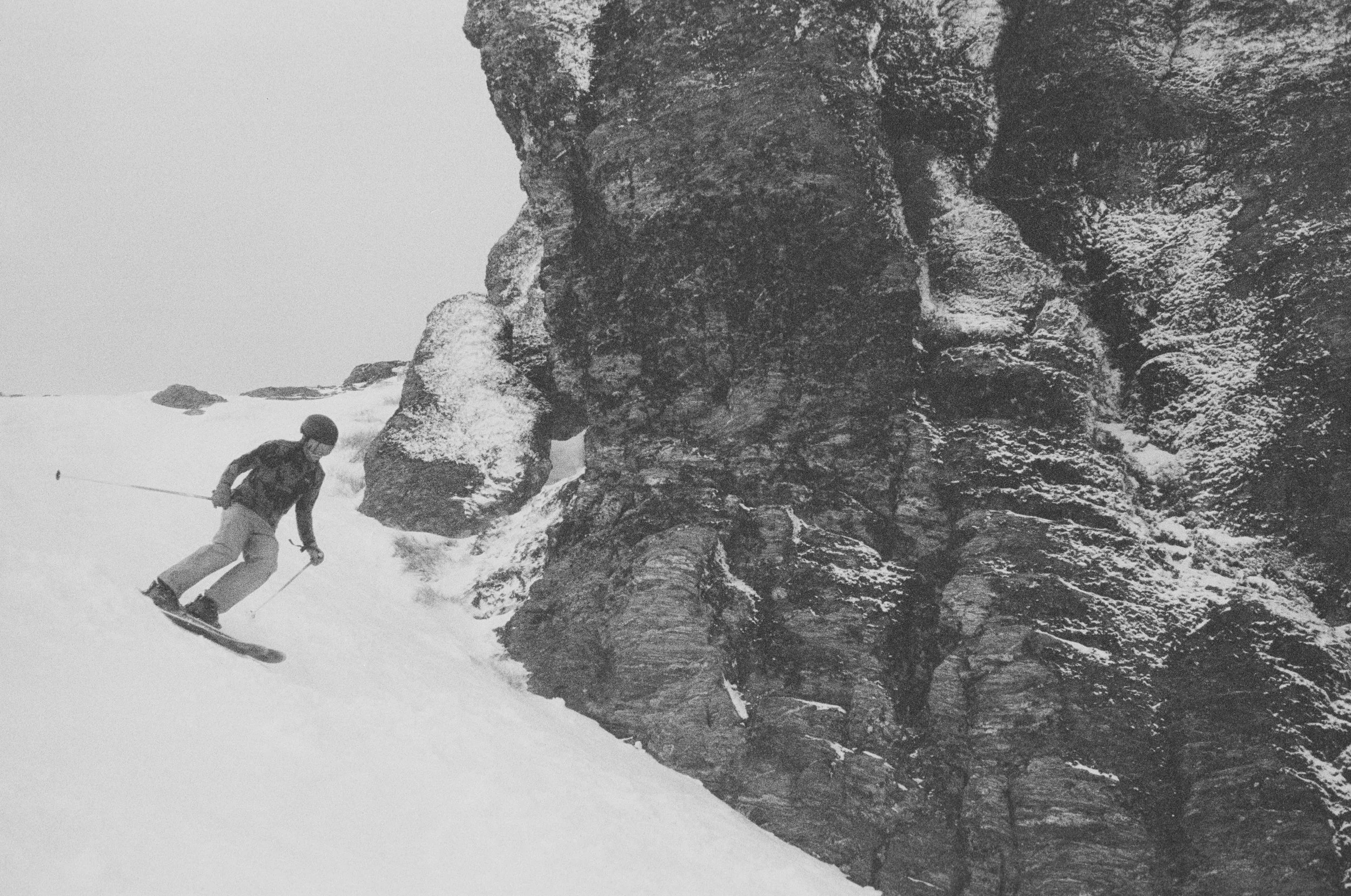 A person skiing down a snowy slope near a large rocky mountain in a winter landscape.