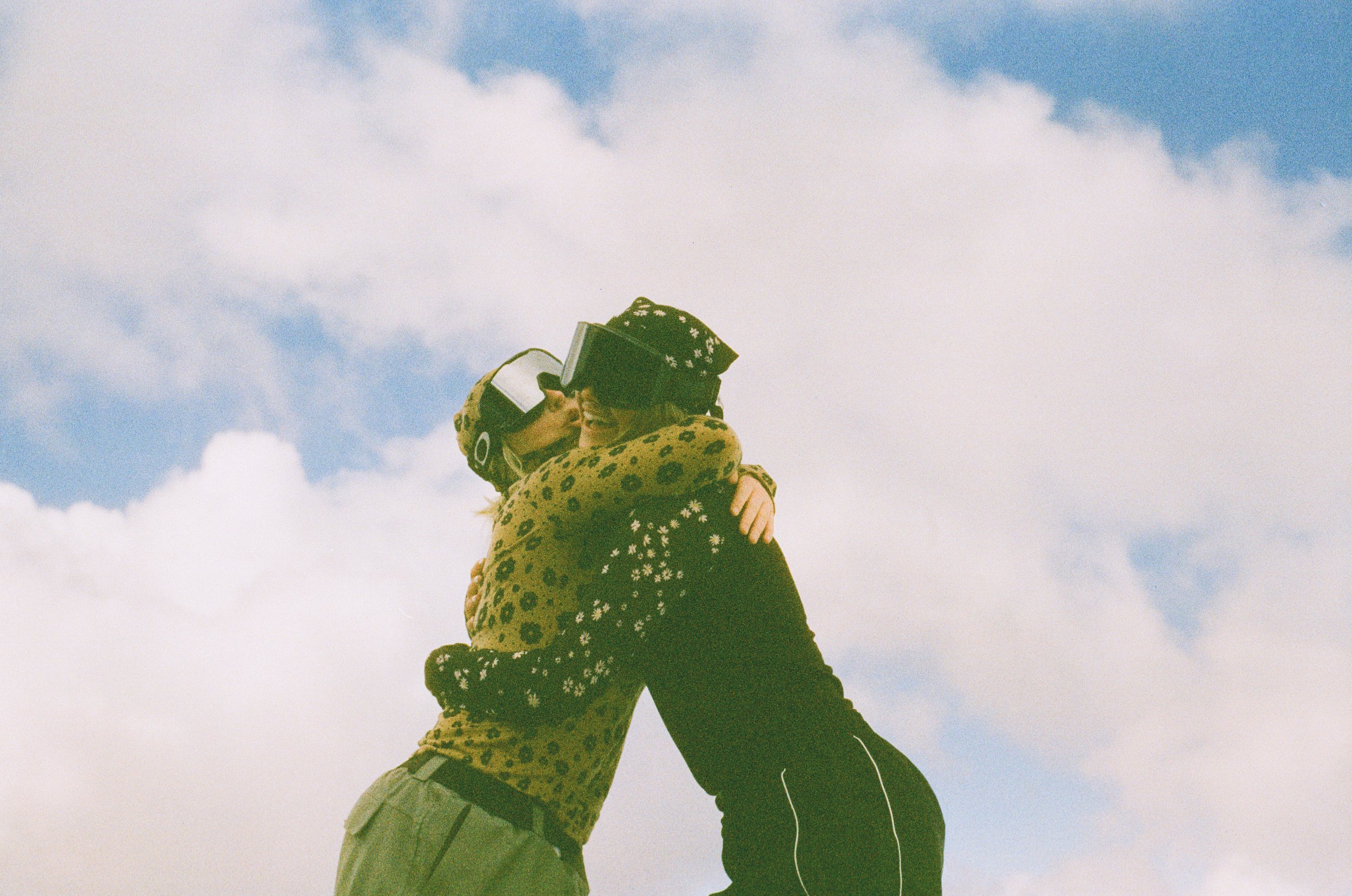 Two people embracing outdoors with a cloudy sky in the background.