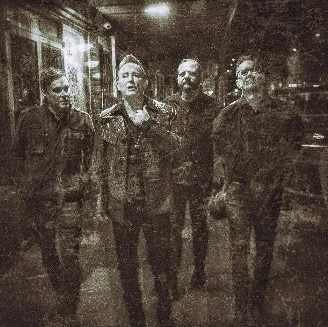 Four men walking on a street at night, photographed in black and white.