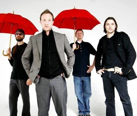 Four men standing in a row holding red umbrellas against a white background.