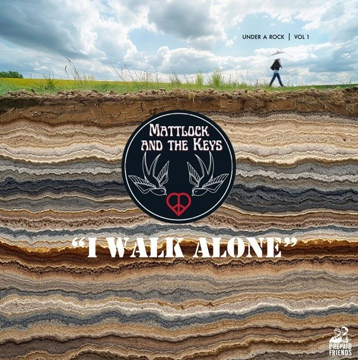Cross-section of layered rock soil beneath a cloudy sky with a person walking in the distance holding an umbrella, and a circular logo reading "Mattlock and the Keys" with a peace symbol and birds, along with the text "I Walk Alone" and the label "Under a Rock Vol 1".